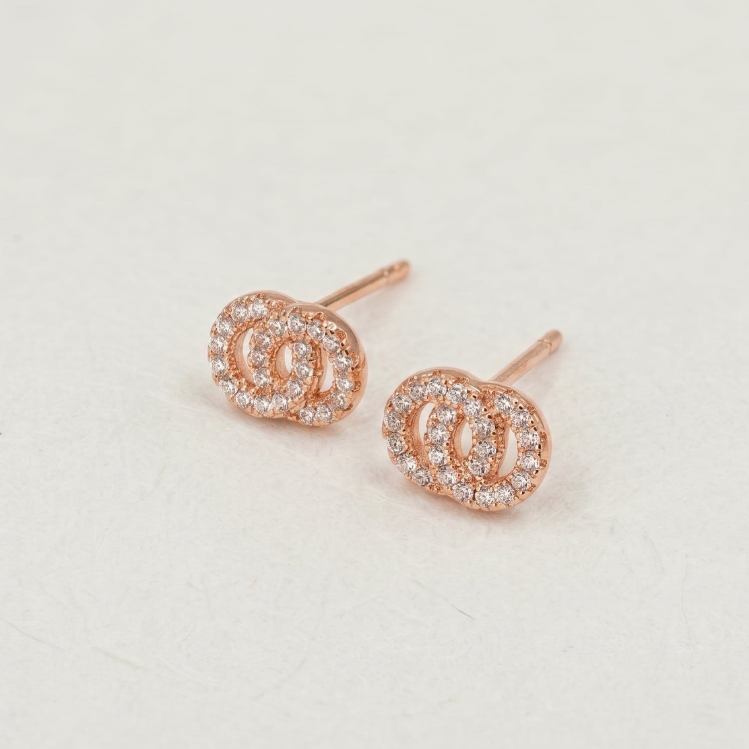 Rose gold vermeil stud earrings featuring two interlocking circle designs embellished with sparkling clear stones, showcasing a modern and delicate jewellery style.