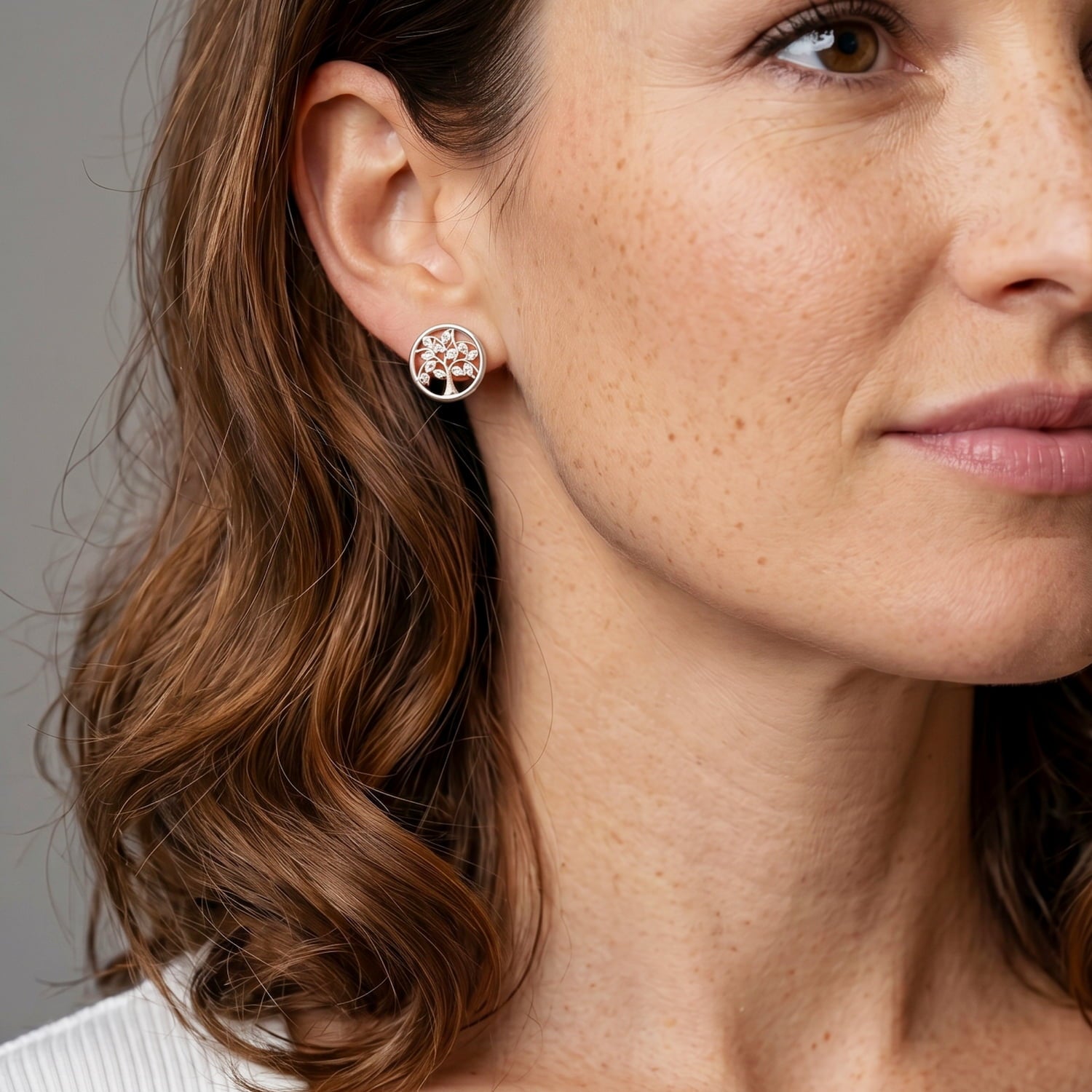 Sterling silver stud earrings featuring a sculptural tree design encased within a polished circular frame, worn on the ear for a refined and contemporary look.