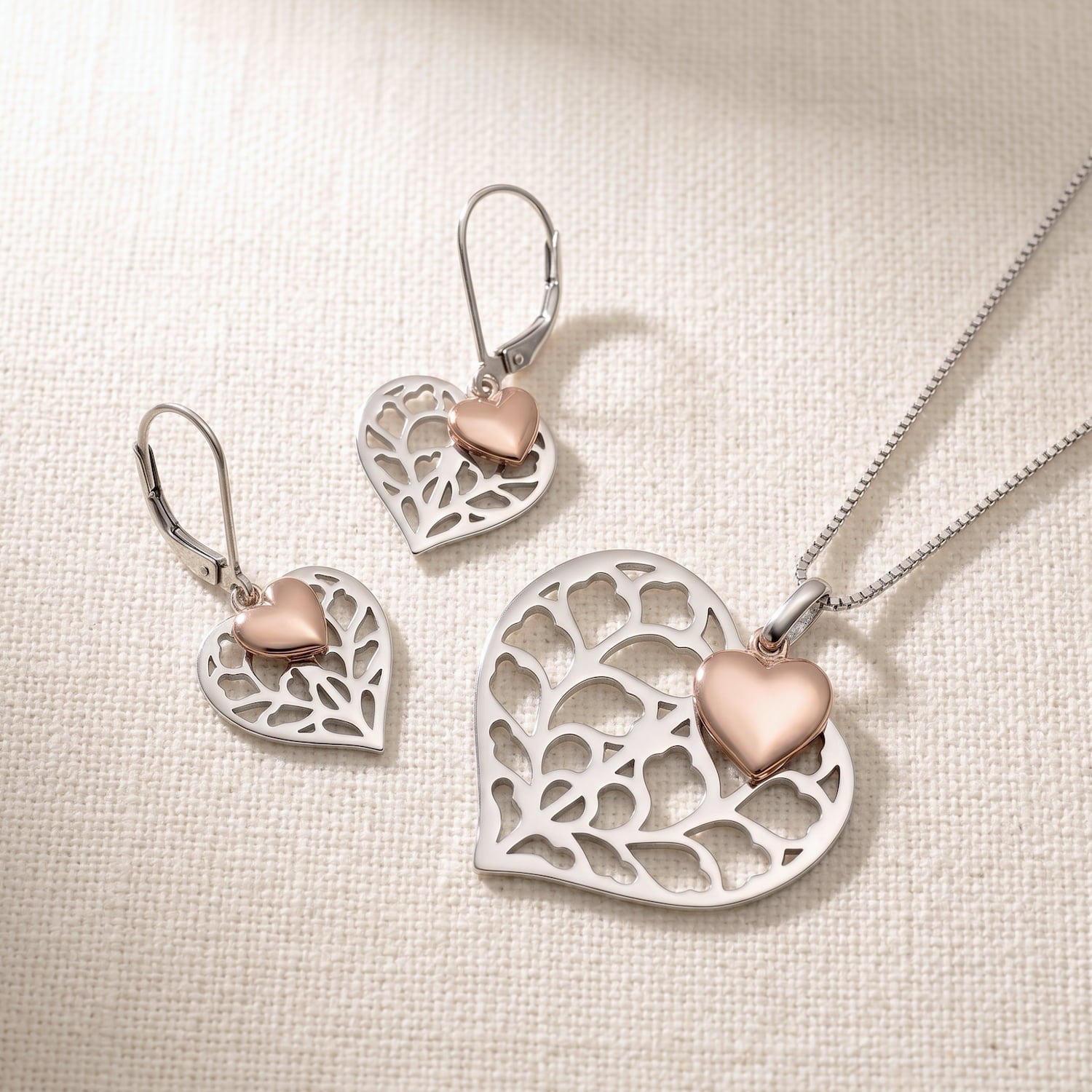 A matching set of sterling silver necklace and earrings featuring a sculptural openwork heart pendant accented with a small rose gold vermeil heart.