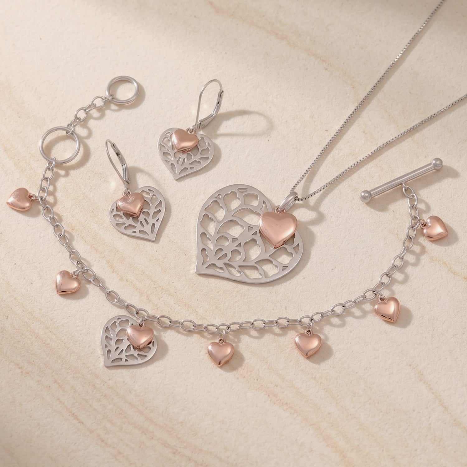 A matching set of sterling silver necklace, bracelet and earrings featuring a sculptural openwork heart pendant accented with a small rose gold vermeil heart.