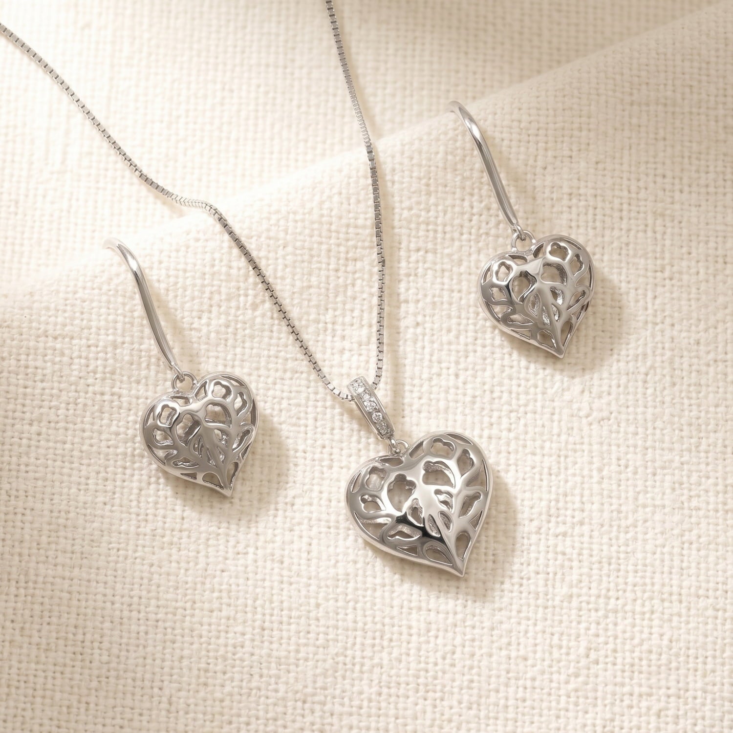 Sterling silver drop earrings and matching pendant featuring delicate openwork hearts with intricate leaf-inspired cut-out patterns on a fine chain.