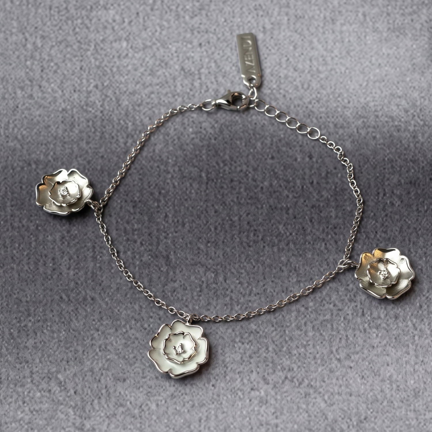 Delicate sterling silver bracelet featuring three Yorkshire rose charms with white enamel accents, showcasing a refined and sculptural design in contemporary silver jewellery by Azendi.