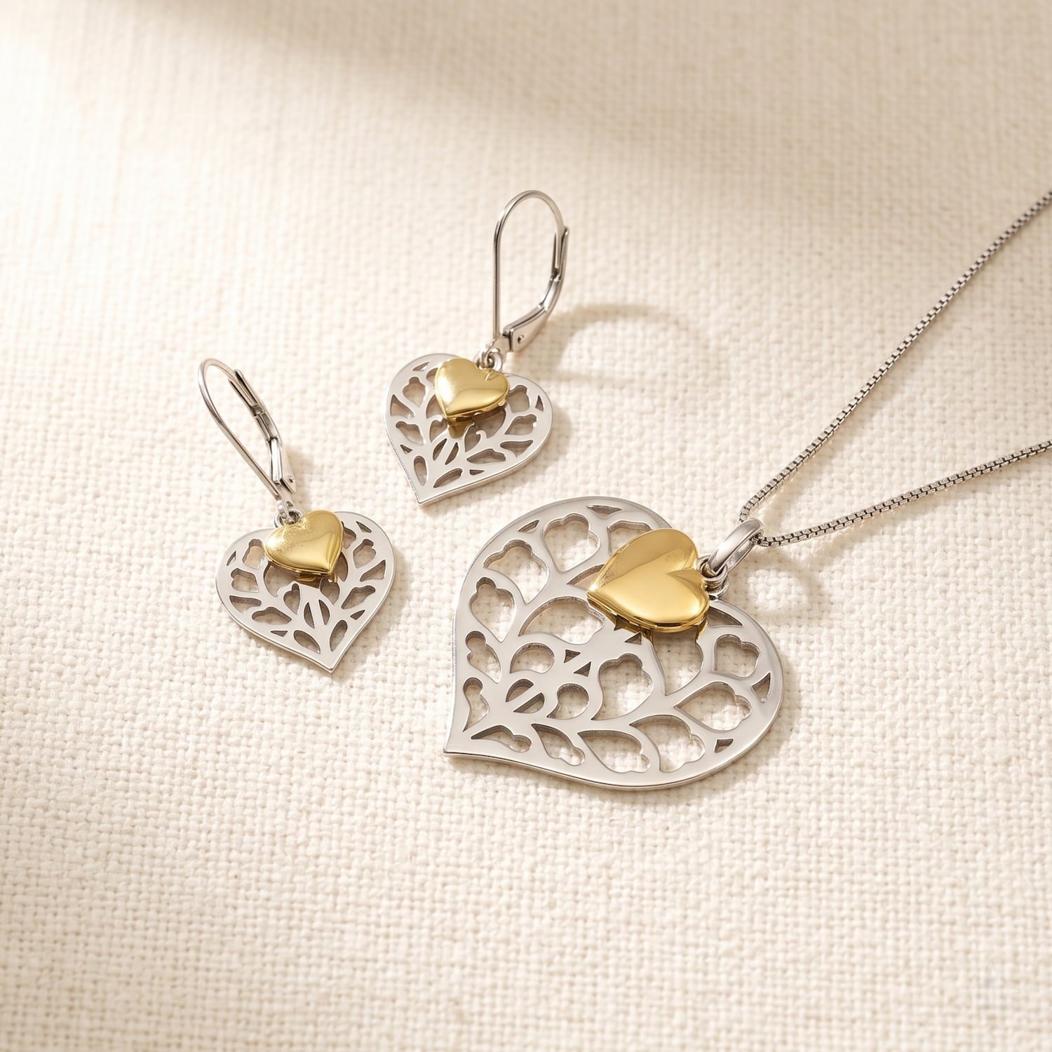 A matching set of sterling silver drop earrings and pendant featuring openwork heart designs with polished gold vermeil heart accents, secured by lever-back clasps for elegant wear.