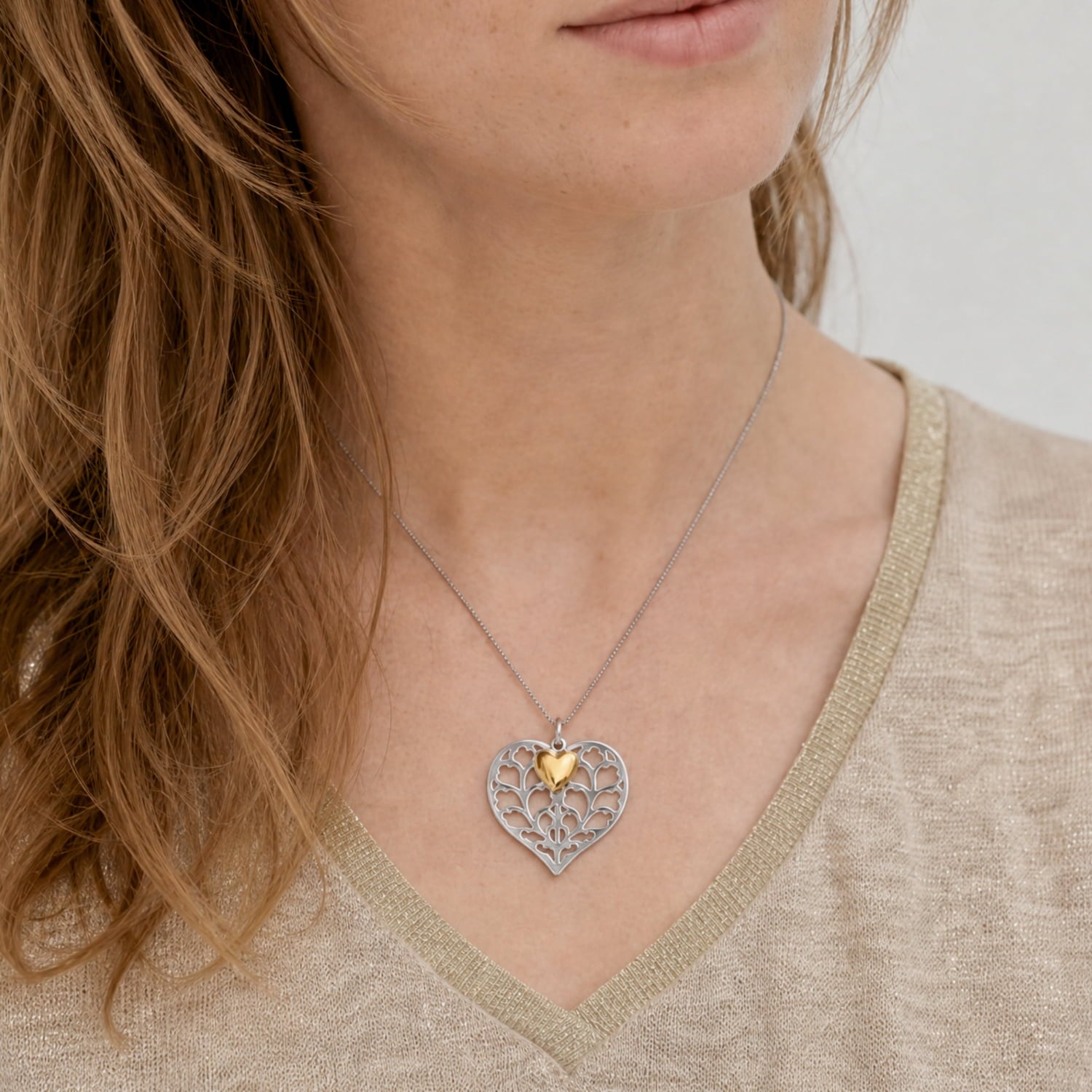 Model wears sterling silver heart pendant featuring an intricate filigree design with a small yellow gold vermeil heart accent, suspended on a fine silver chain worn with a crisp white shirt.