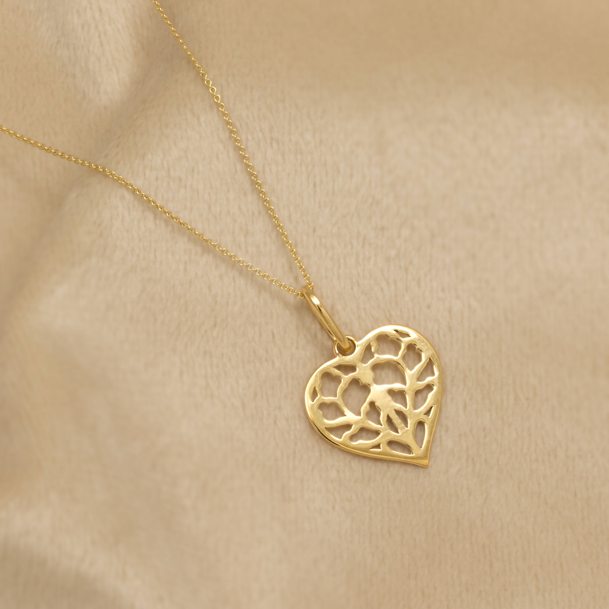 9 carat yellow gold heart-shaped pendant featuring an openwork design inspired by York Minster with a delicate, sculptural finish placed on a cream velvet cloth.
