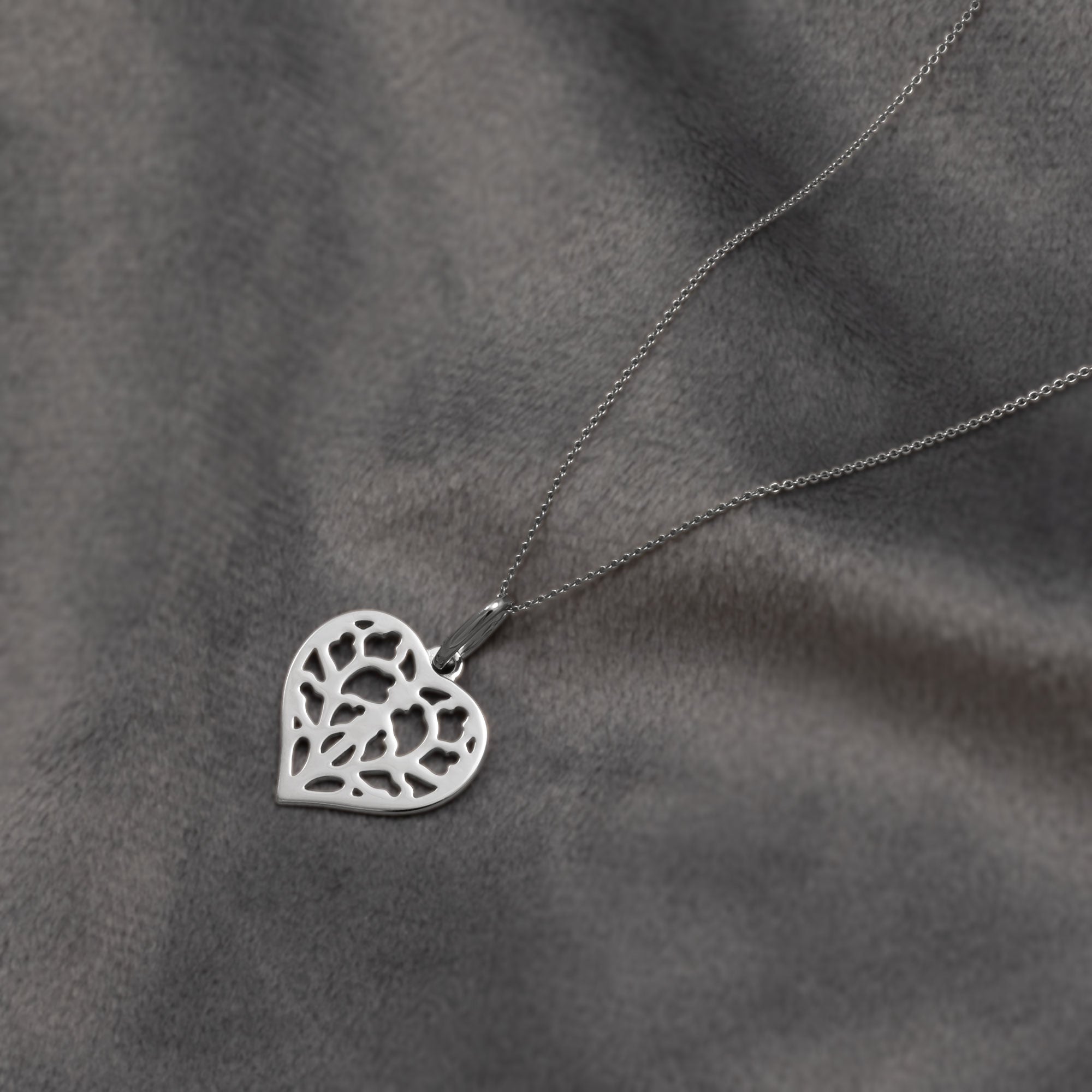 Delicate 9 carat white gold heart pendant featuring an openwork York Minster motif suspended on a fine chain, exemplifying refined contemporary jewellery design. Placed on a grey velvet cloth.
