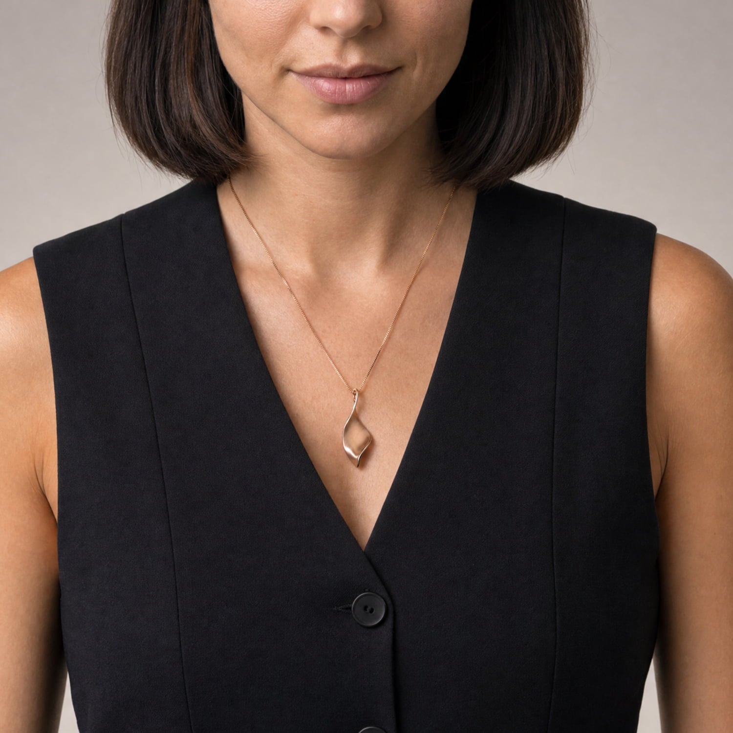 A close-up of a woman wearing a rose gold twisting pendant, styled with a black sleeveless top against a neutral background.