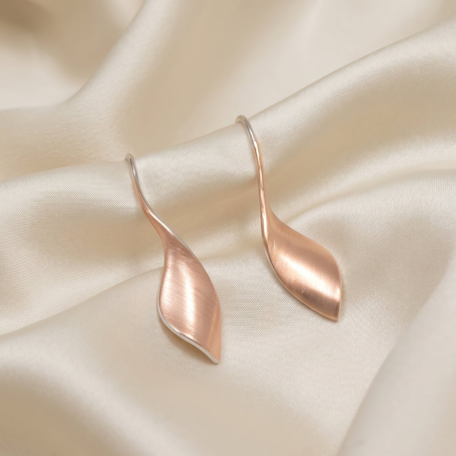 A pair of rose gold vermeil twisting drop earrings on a cream silk background