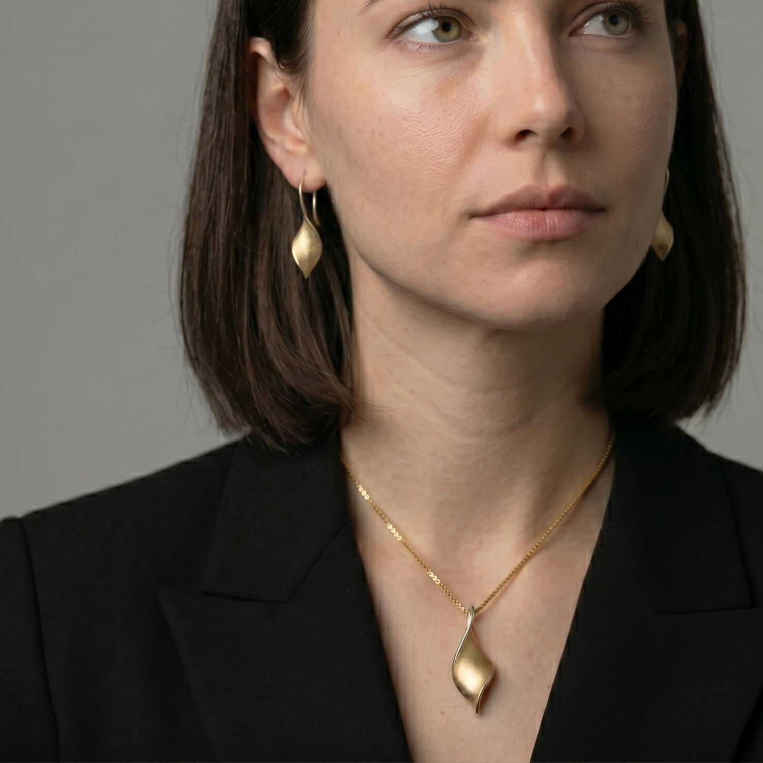Woman in black blazer wears yellow gold vermeil twist pendant and earrings