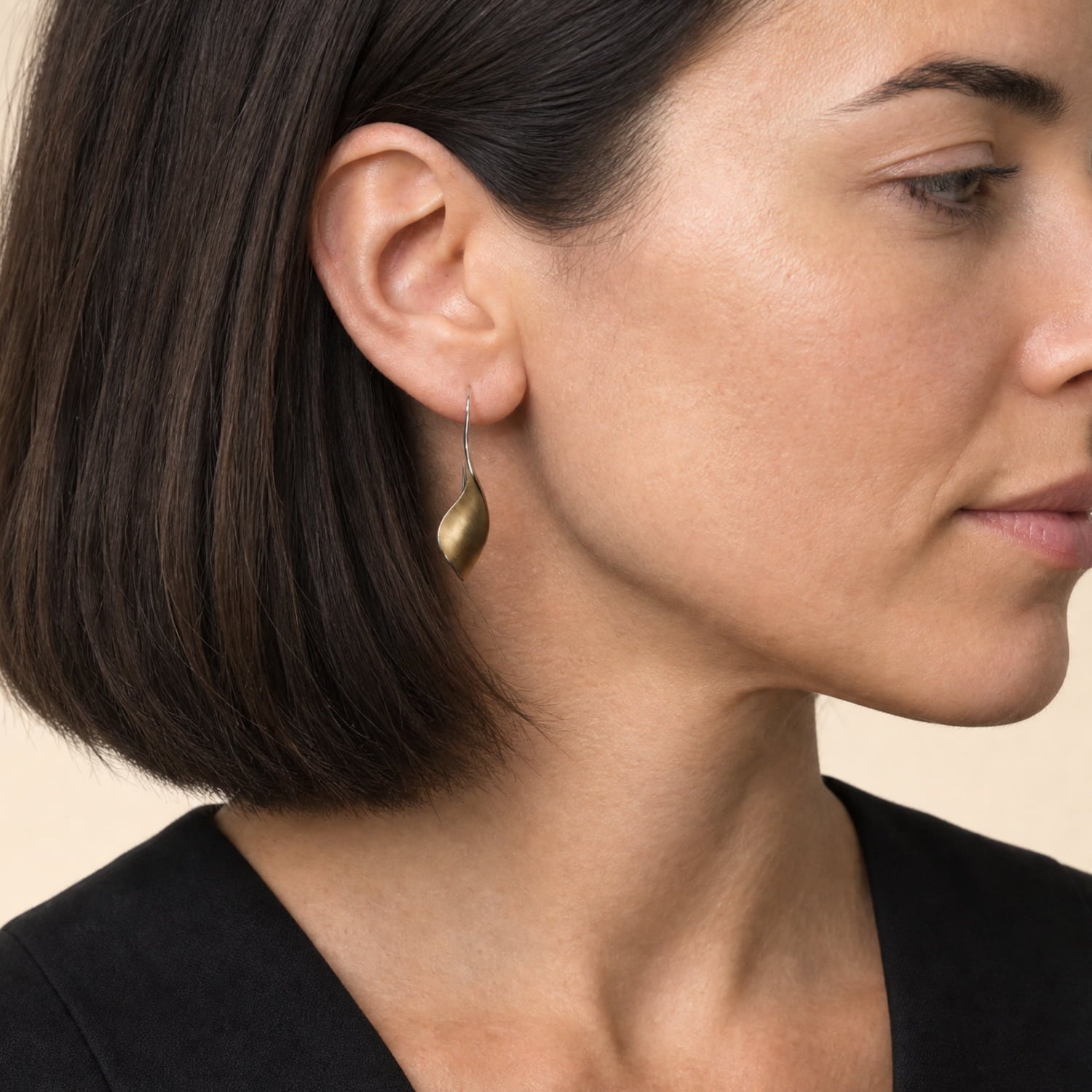A close-up side profile of a woman with a dark bob haircut wearing a twisting gold vermeil earring.