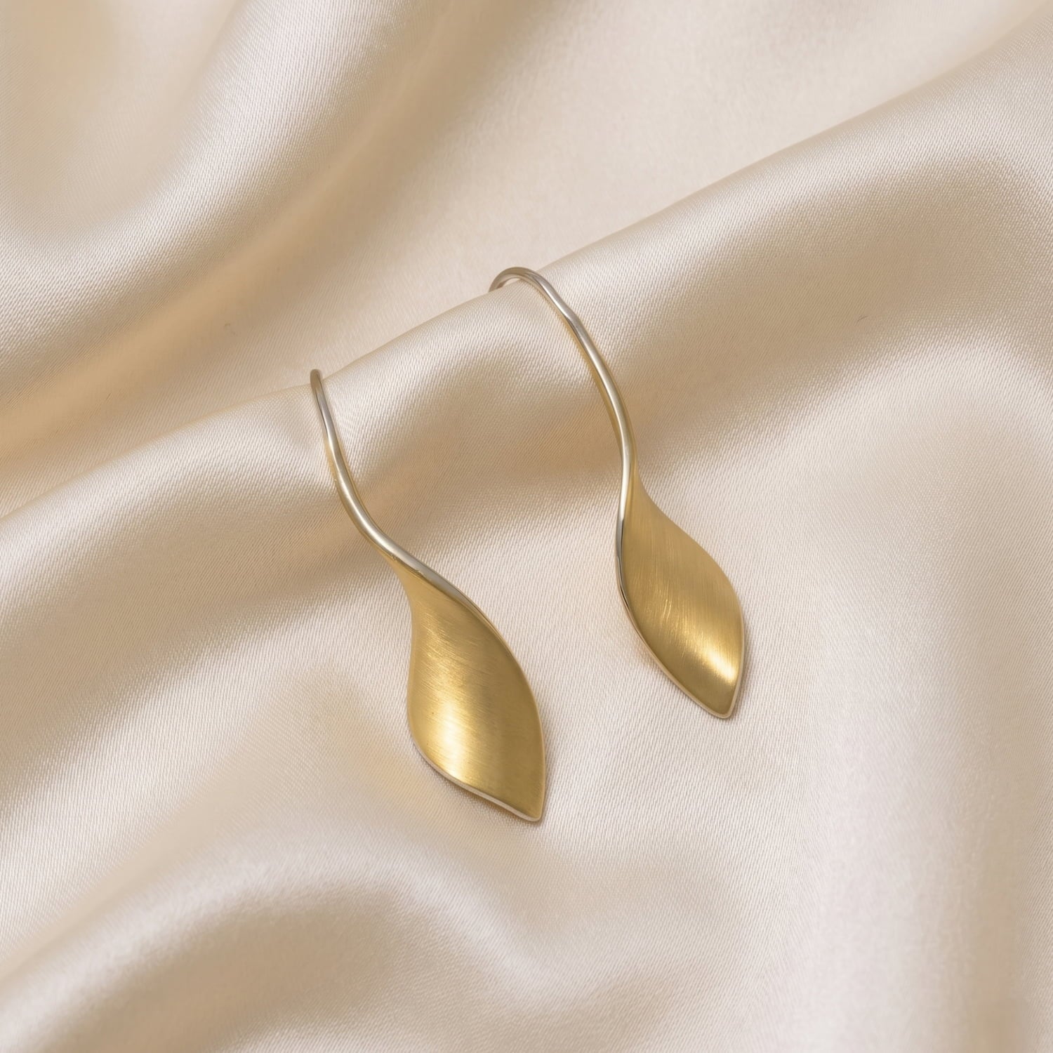 A pair of yellow gold vermeil twist drop earrings with satin finish on a silk background