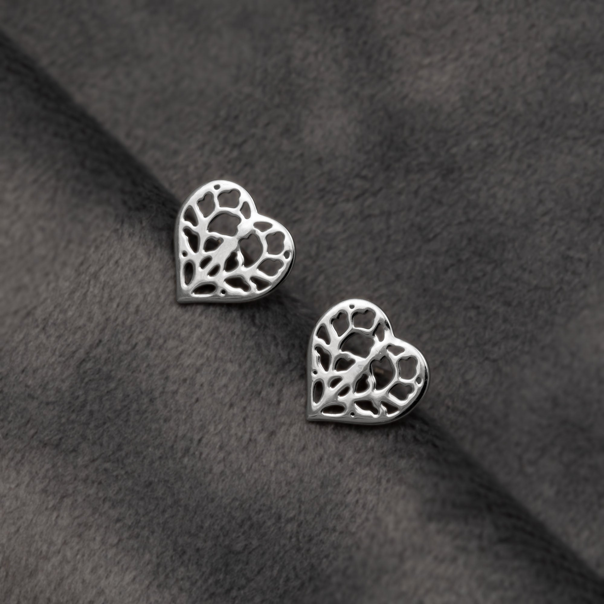 Pair of 9 carat white gold stud earrings featuring delicate openwork heart shapes inspired by York Minster, combining polished surfaces with a refined sculptural design. Placed on a grey velvet cloth.