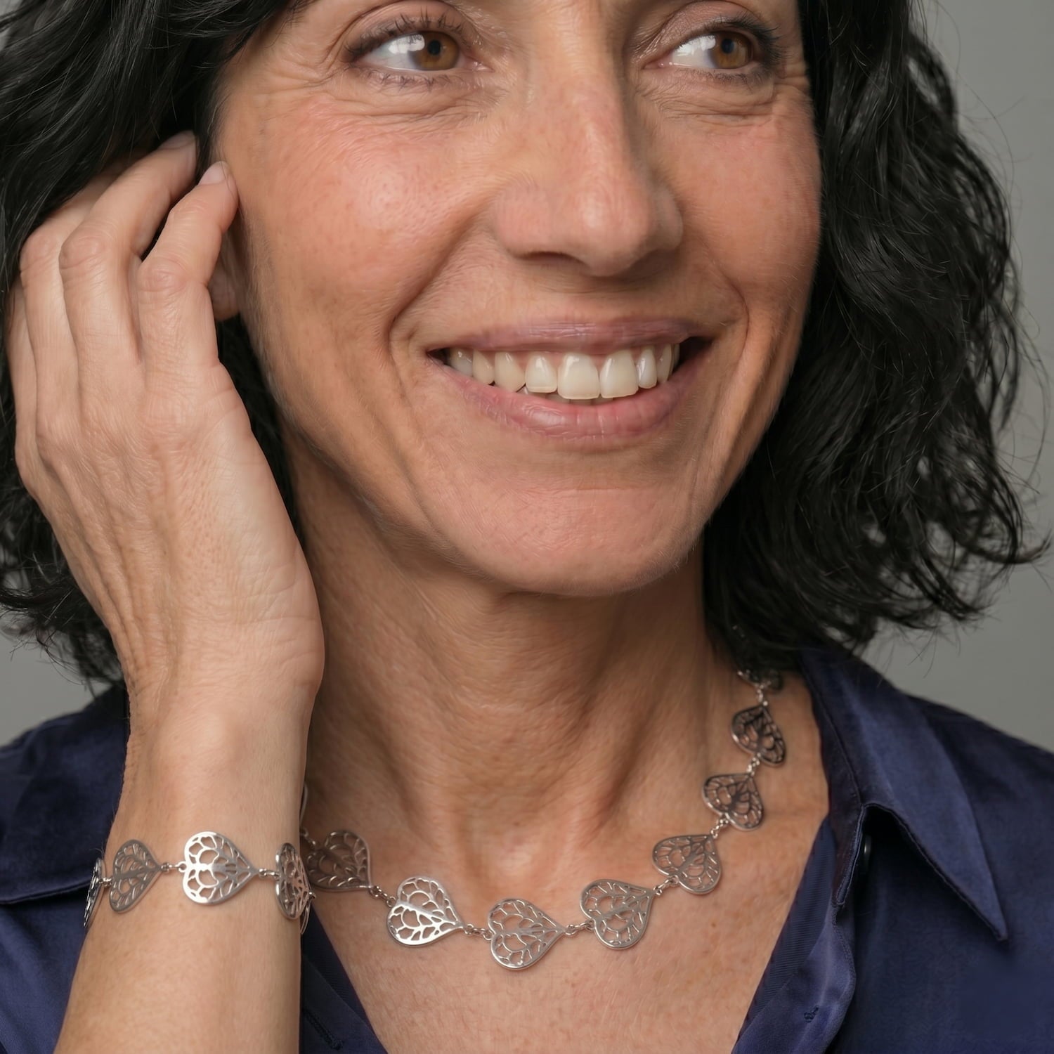 Sterling silver bracelet and necklace with alternating openwork and polished heart links, showcasing a sculptural design inspired by Yorkshire, worn with a navy silk blouse.