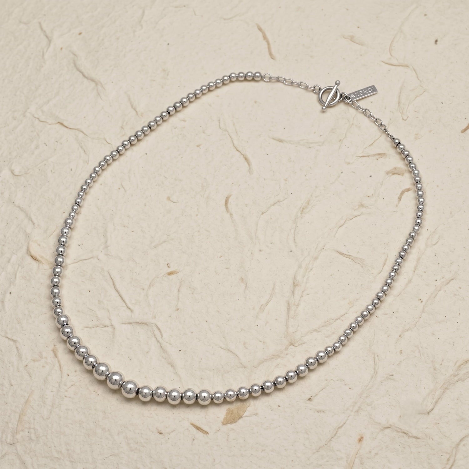 Silver beaded necklace on a textured beige background
