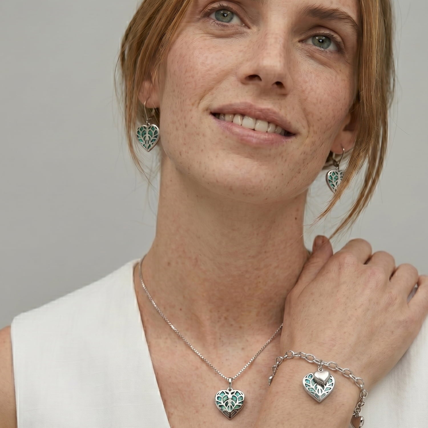 Model wears a silver T-bar bracelet featuring a heart design with abalone mother of pearl detailing, accompanied by small heart charms and a toggle clasp.
