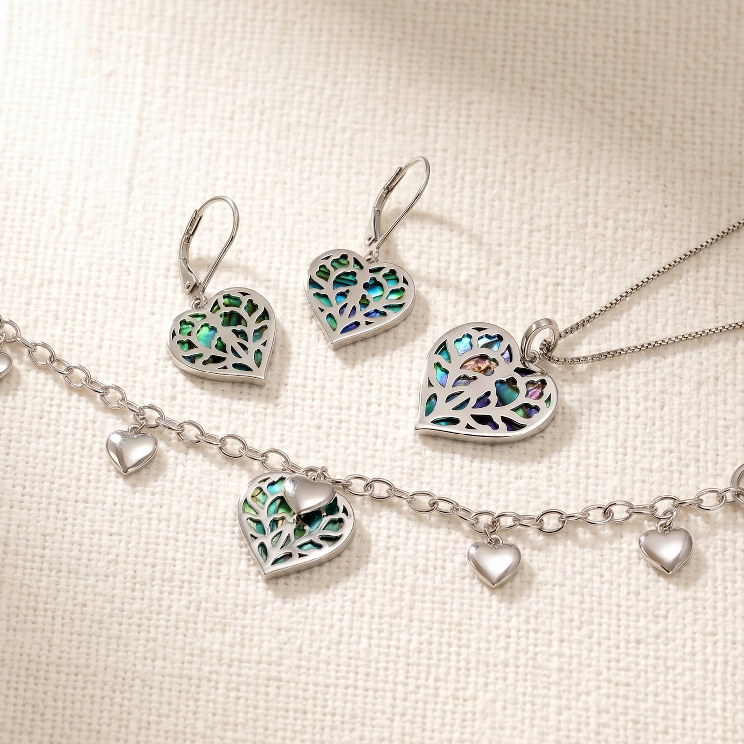 Sterling silver necklace, bracelet, and earrings set featuring sculptural heart-shaped designs with abalone inlay, showcasing delicate openwork and polished charm accents.
