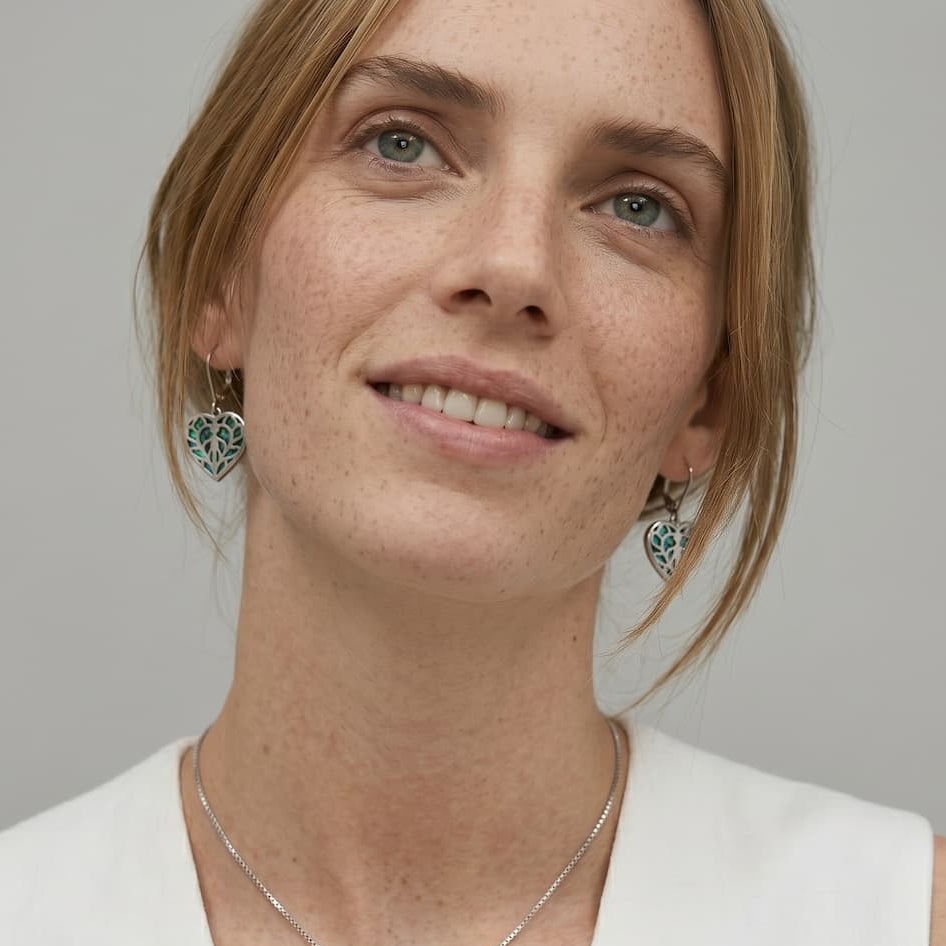 Close-up of a woman wearing sterling silver earrings with heart-shaped abalone inlays featuring intricate cut-out detailing, highlighting expert British craftsmanship.