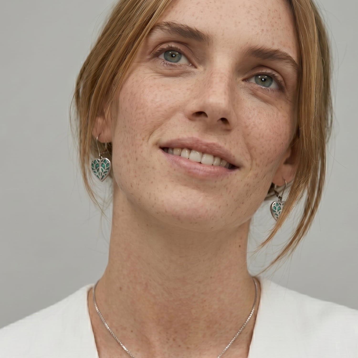 Close-up of a woman wearing sterling silver earrings with heart-shaped abalone inlays featuring intricate cut-out detailing, highlighting expert British craftsmanship.