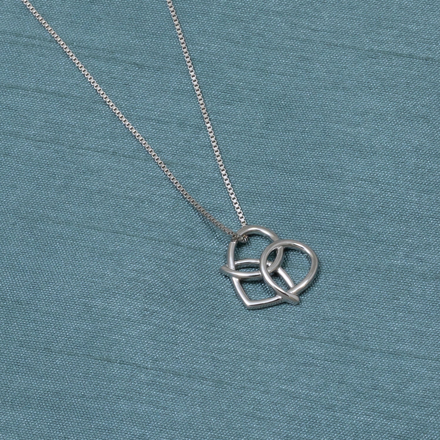 Sterling silver pendant featuring an interwoven Celtic trinity heart design suspended from a fine chain, embodying elegant and sculptural contemporary silver jewellery.