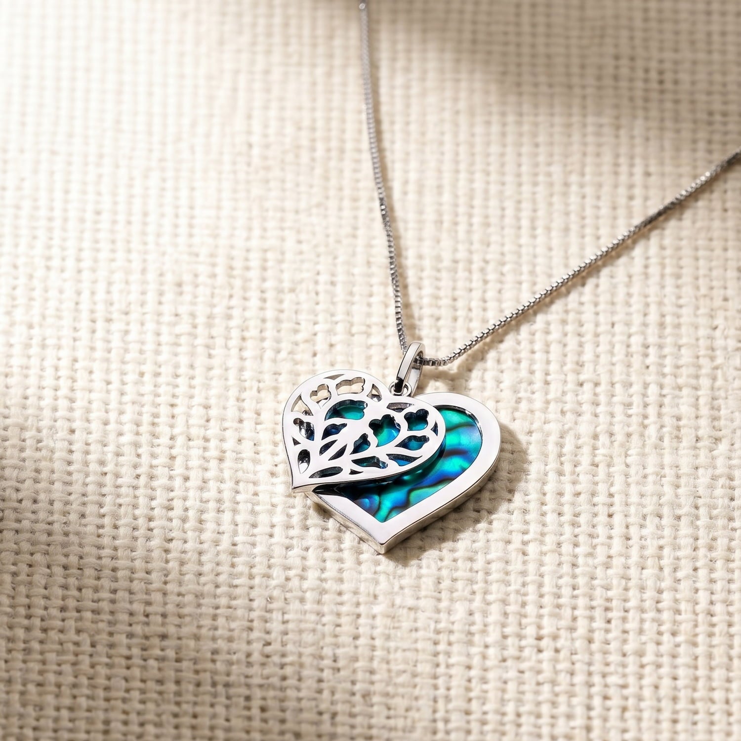 Sterling silver necklace featuring a double heart pendant with a cut-out filigree overlay and an iridescent abalone background, crafted for elegant everyday wear.