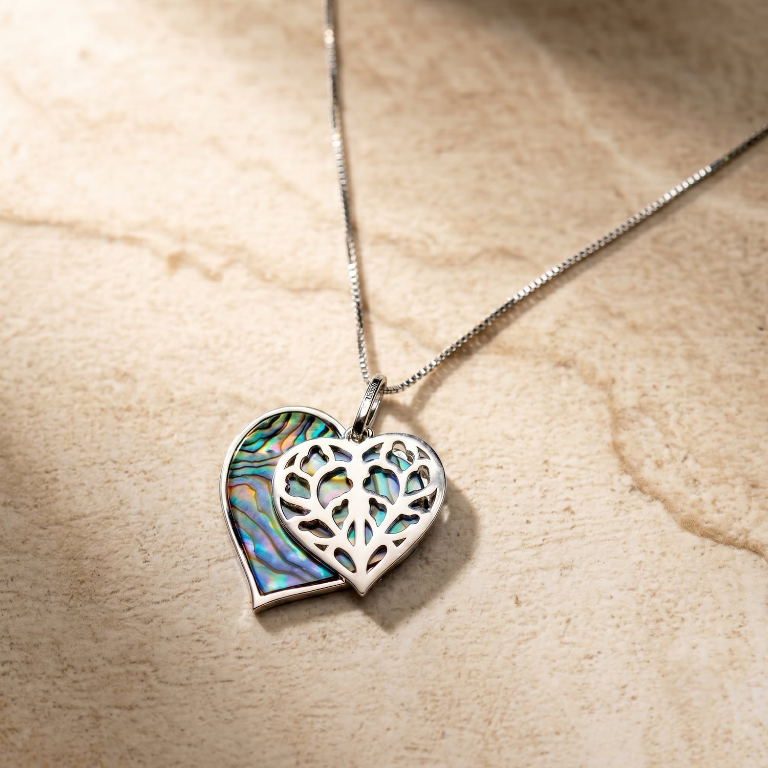 Sterling silver double heart pendant featuring an intricate filigree heart layered over a vibrant abalone shell heart, suspended on a fine silver chain.