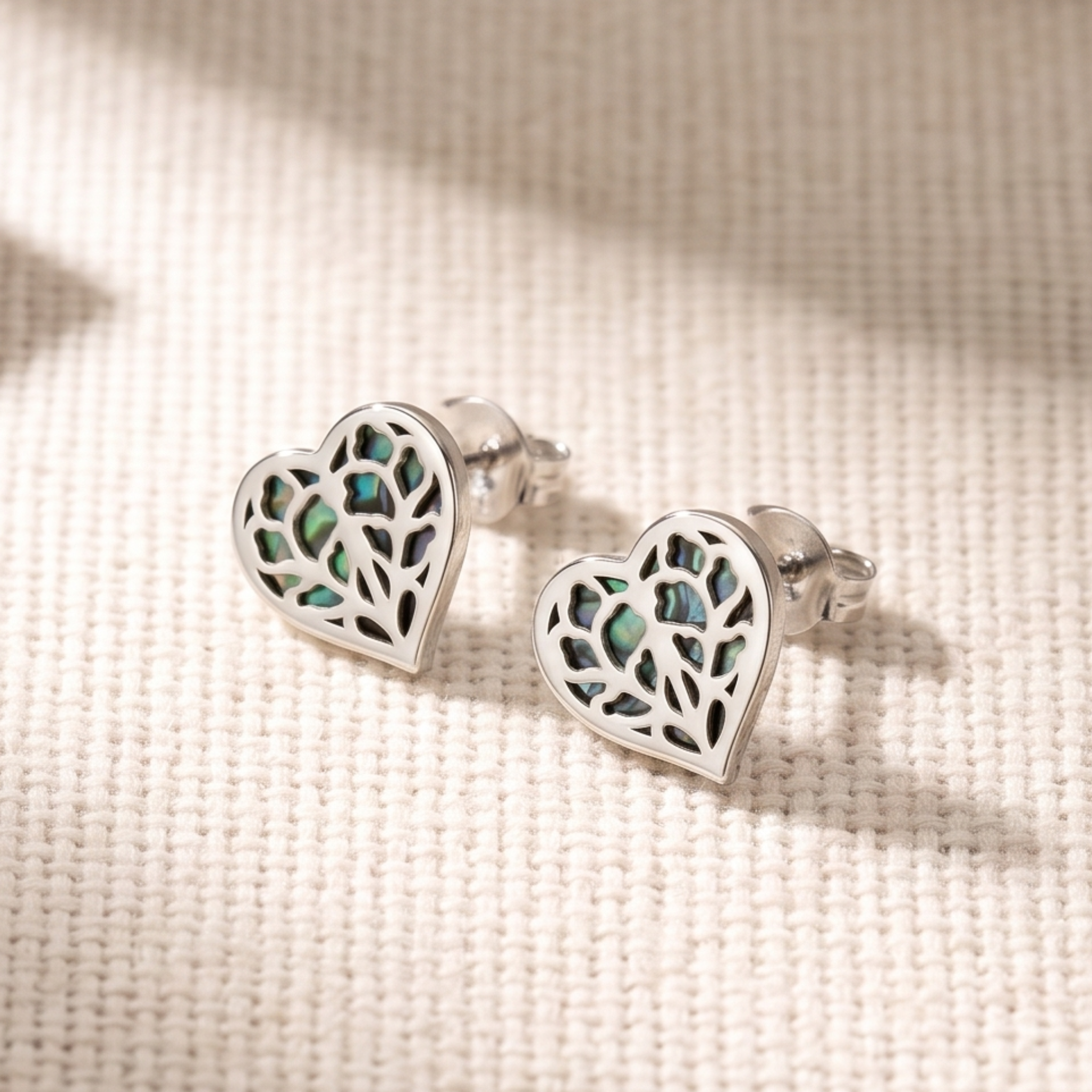Pair of sterling silver heart-shaped stud earrings with intricate cut-out detailing revealing iridescent abalone inlay, showcasing elegant and contemporary design.