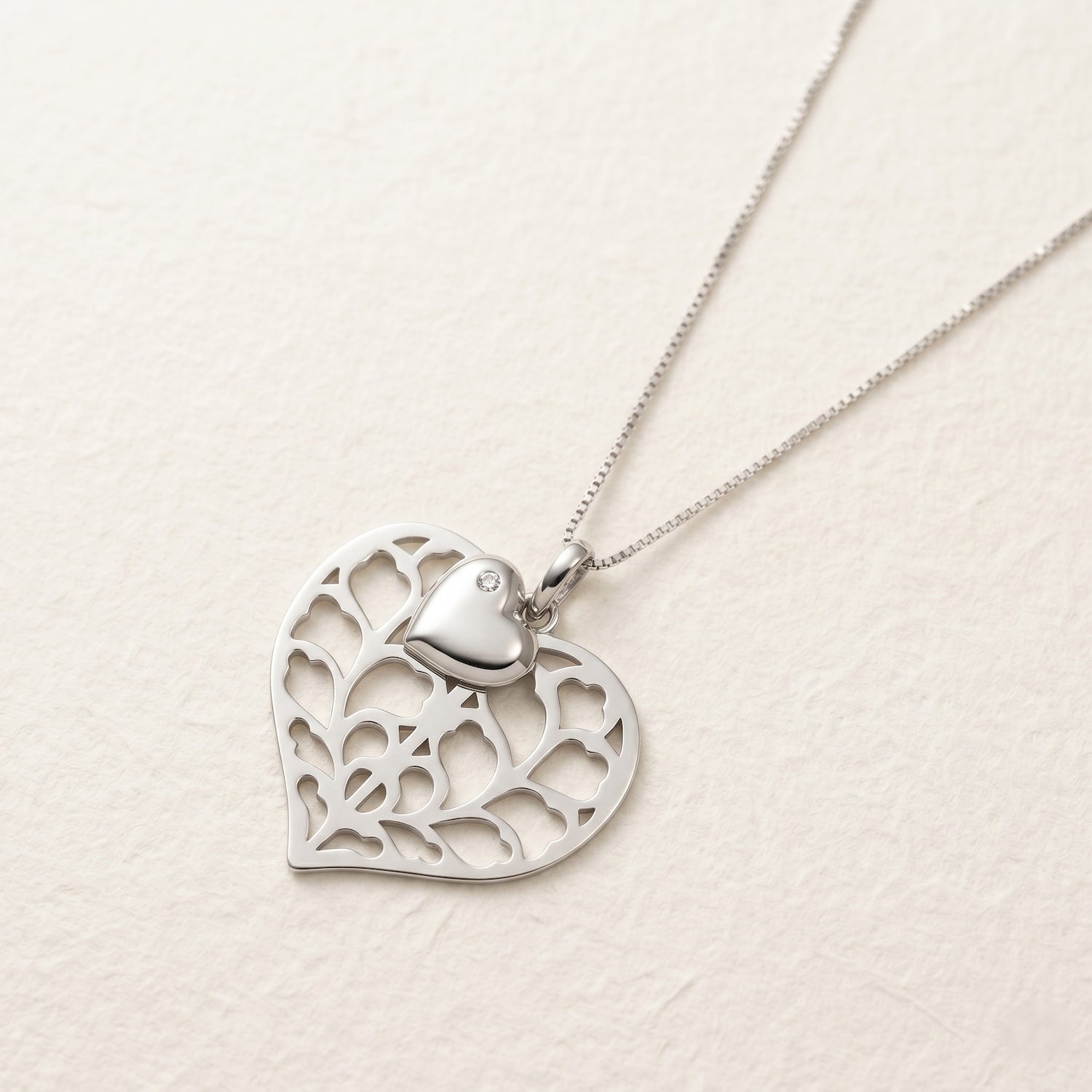 Sterling silver double pendant necklace featuring a solid heart overlaying a sculptural, openwork heart design, displayed on a fine chain against a textured surface.