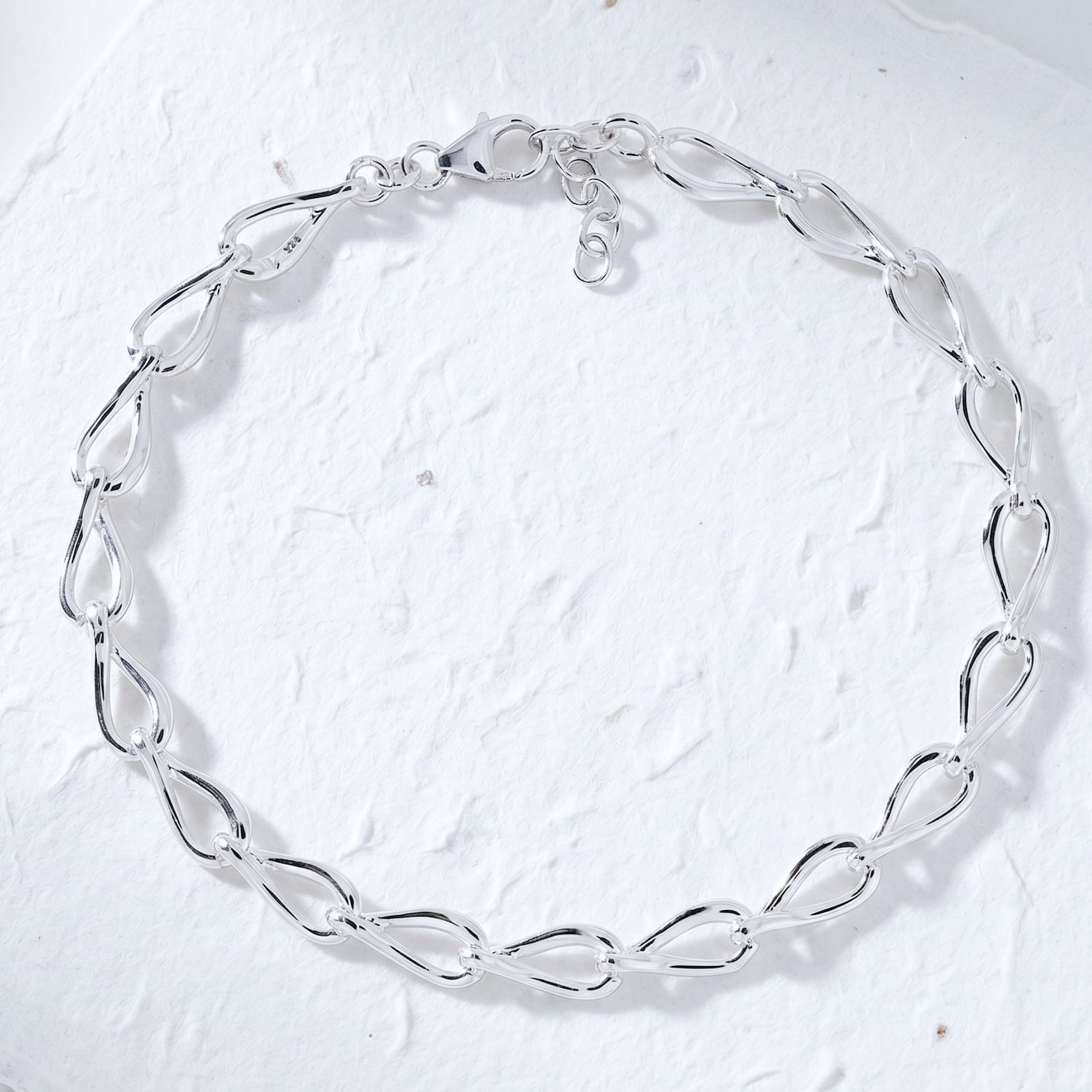 Silver teardrops link bracelet on paper background.