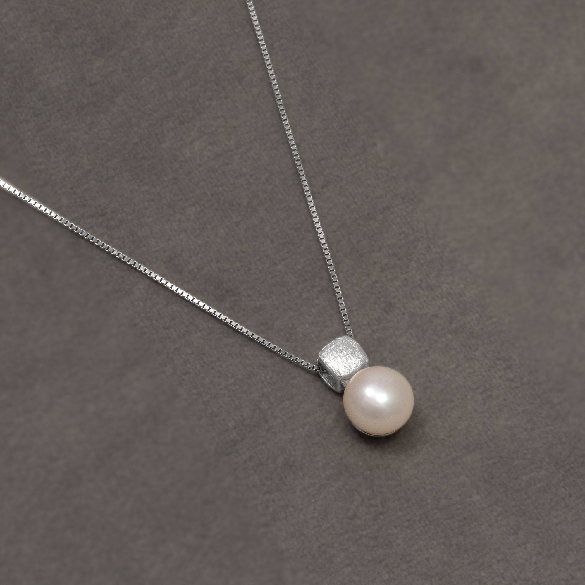 Sterling silver necklace featuring a cubist-inspired pendant with a polished freshwater pearl drop, suspended from a fine chain for a modern, elegant look. Placed on a grey velvet cloth.