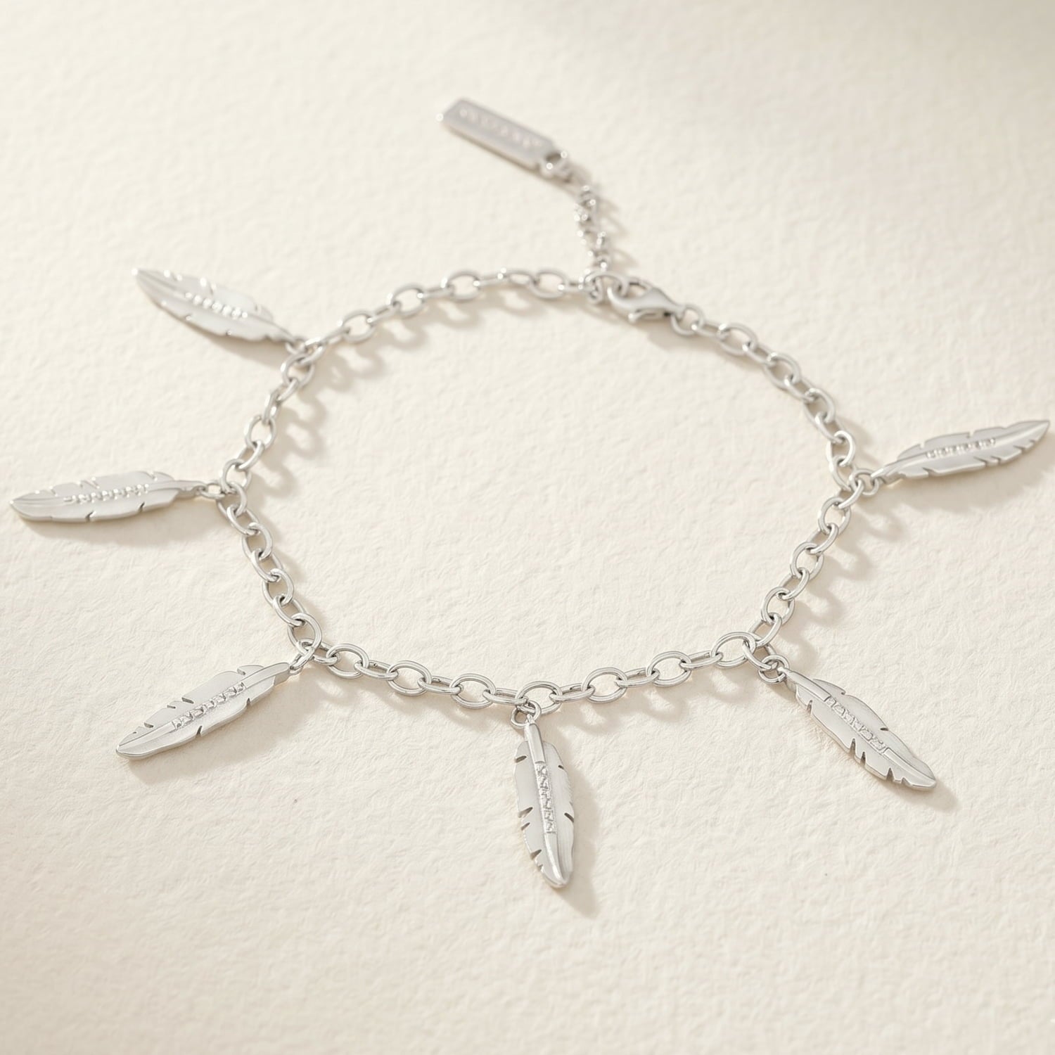 A silver bracelet with frosted feather charms and cubic zirconia stones on a polished belcher chain.