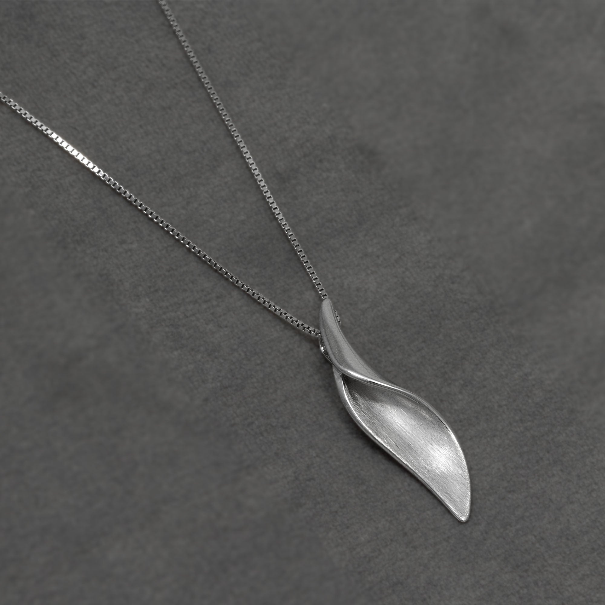 A silver necklace with a textured, leaf-like spiral pendant on a dark grey textured background.