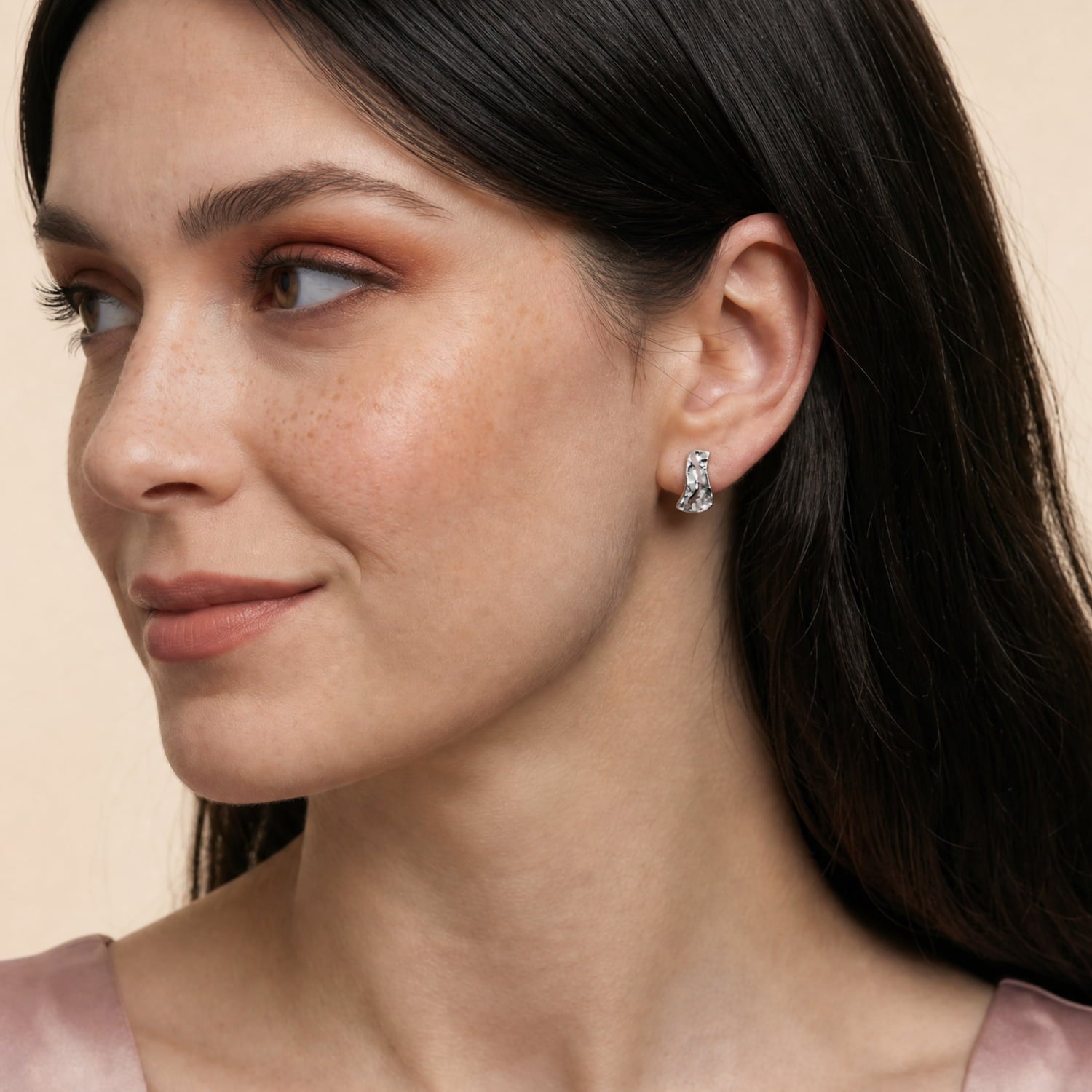 Model wears sterling silver stud earrings with a sculptural, textured design inspired by natural water formations, showcasing smooth and hammered surfaces for a contemporary look.