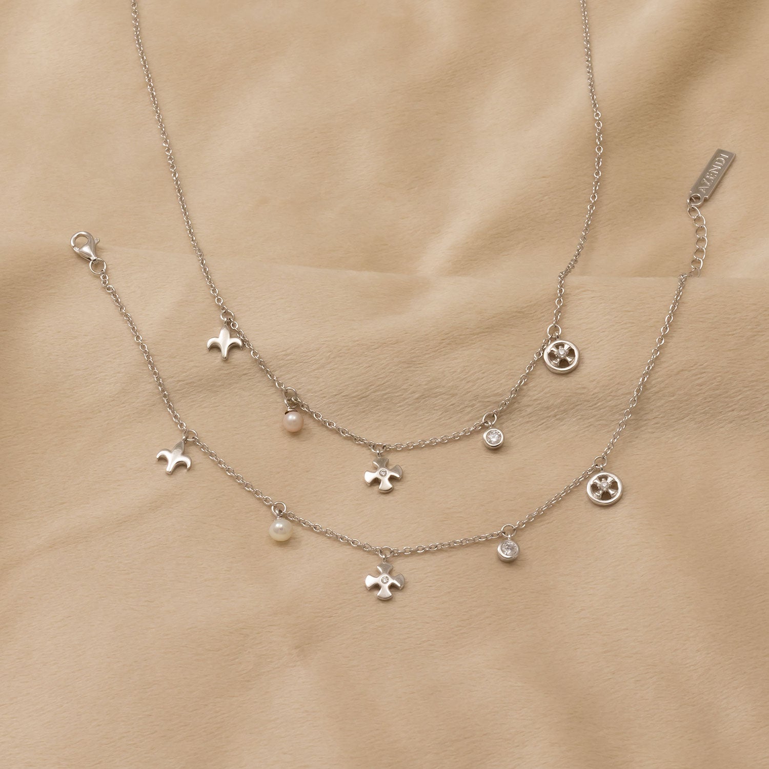 Delicate sterling silver bracelets featuring a mix of fleur de lis charms, small pearls, and sparkling crystal accents, displayed on a soft beige background.