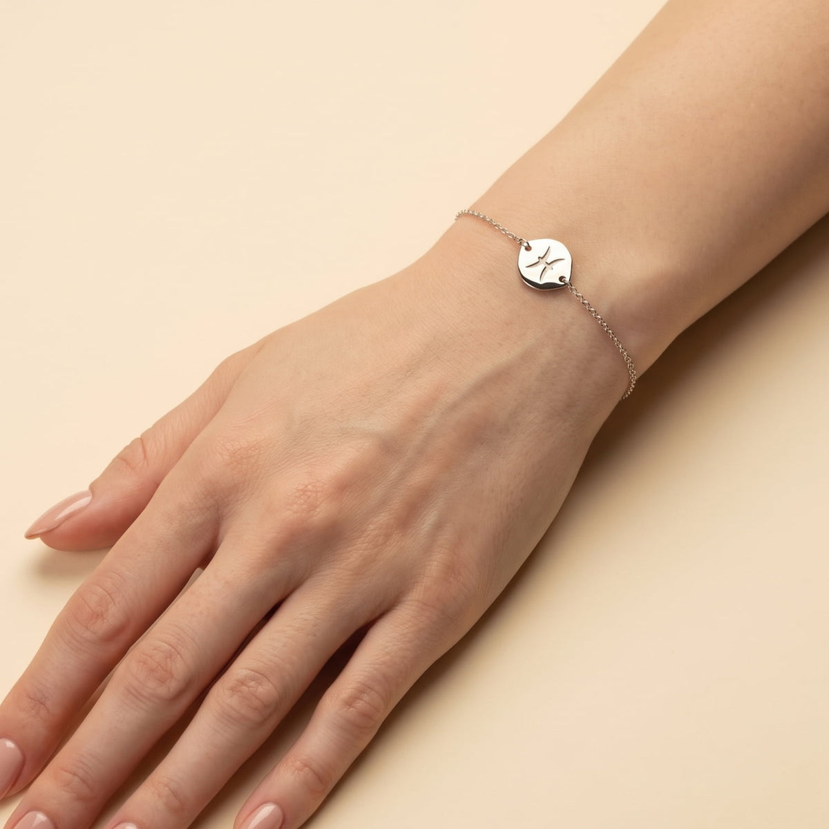 Delicate sterling silver adjustable bracelet featuring a polished Pisces zodiac charm on a fine chain, styled on a wrist against a rich purple background.