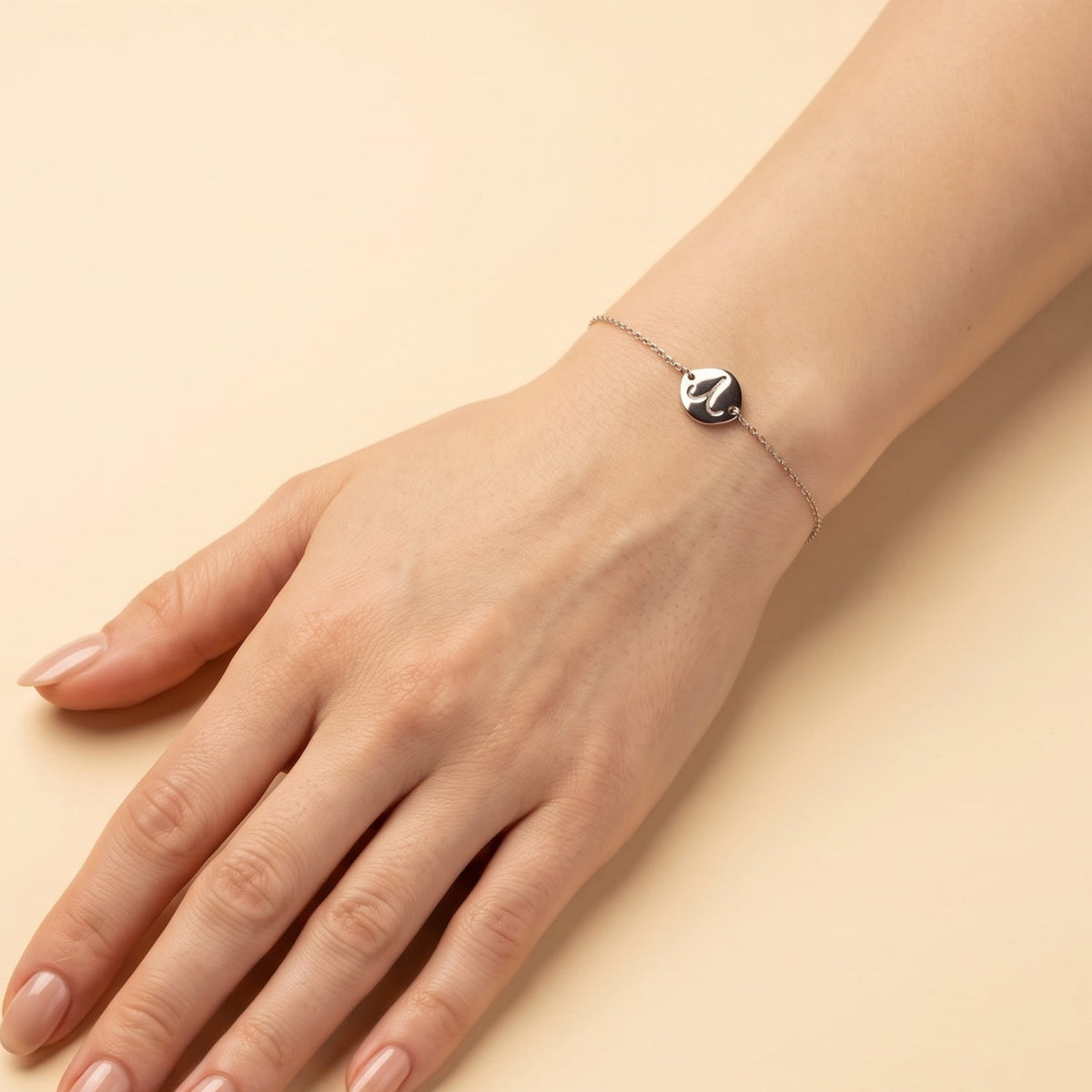 Delicate sterling silver bracelet featuring a sculptural Aries zodiac symbol on a polished disc, with an adjustable sliding bead for a customizable fit, displayed on a wrist.