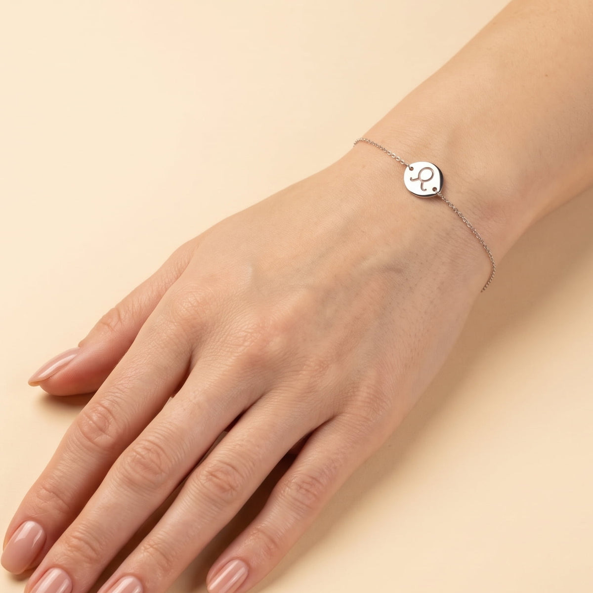 Delicate sterling silver bracelet featuring an adjustable chain with a polished Taurus zodiac symbol disc, styled on the wrist against a cream background.