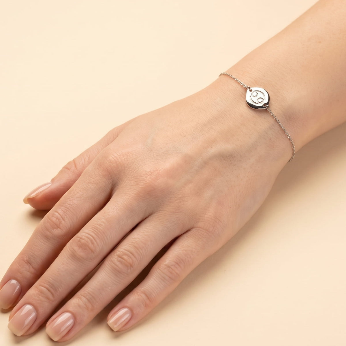 Delicate sterling silver bracelet featuring an adjustable sliding bead and a sculptural Cancer zodiac charm, styled on a wrist against a cream background.