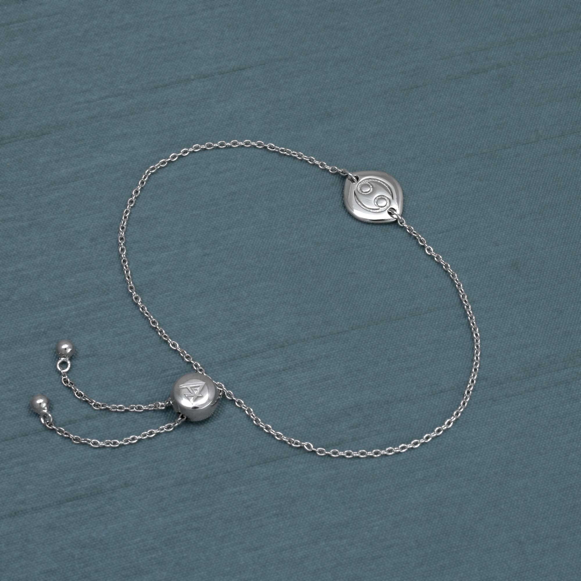 Delicate sterling silver bracelet featuring a sliding adjustable bead and a sculptural Cancer zodiac charm with a polished finish, displayed on a muted blue background.