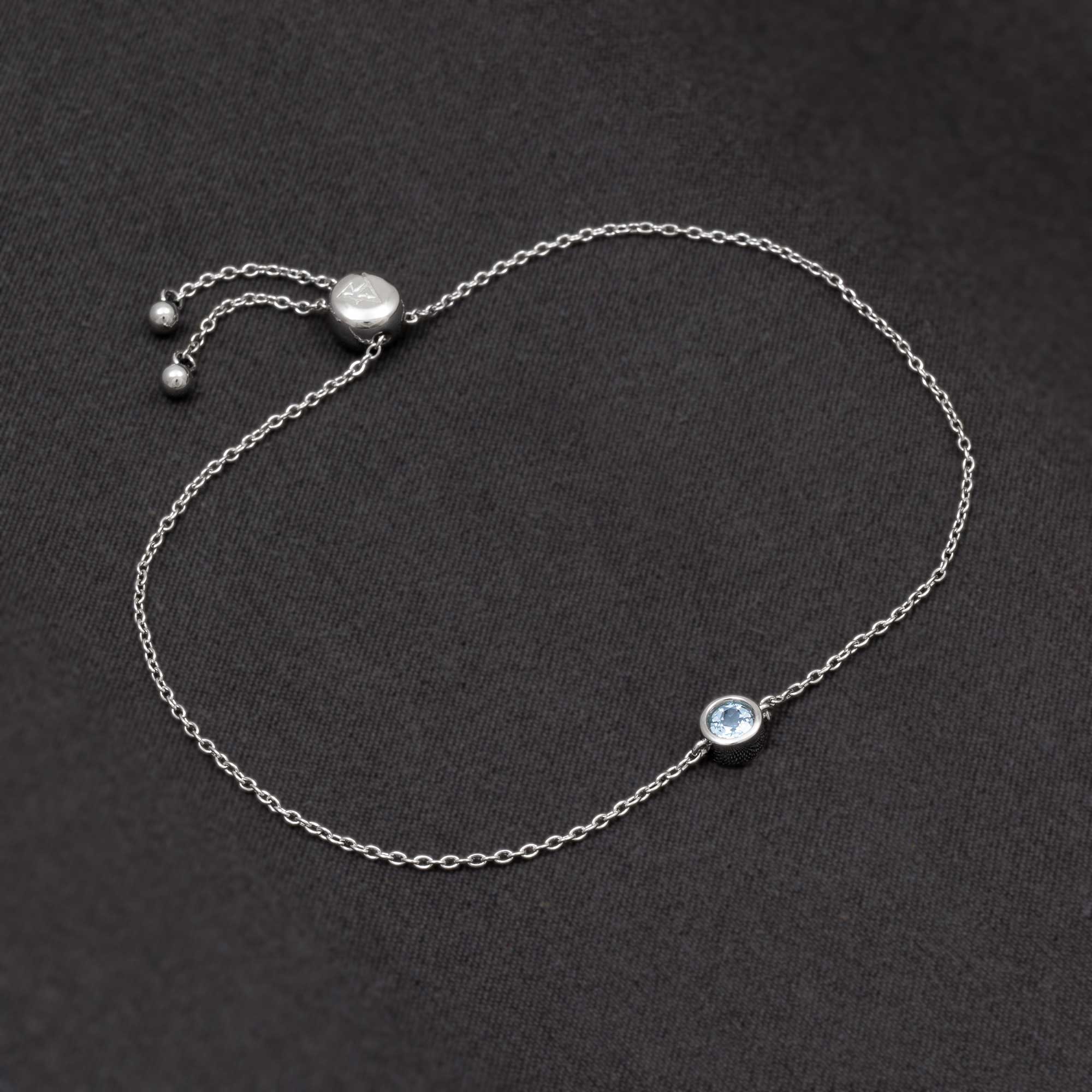Delicate sterling silver bracelet featuring a bezel-set blue topaz birthstone with a sliding adjuster for a customizable fit, showcasing refined British craftsmanship.