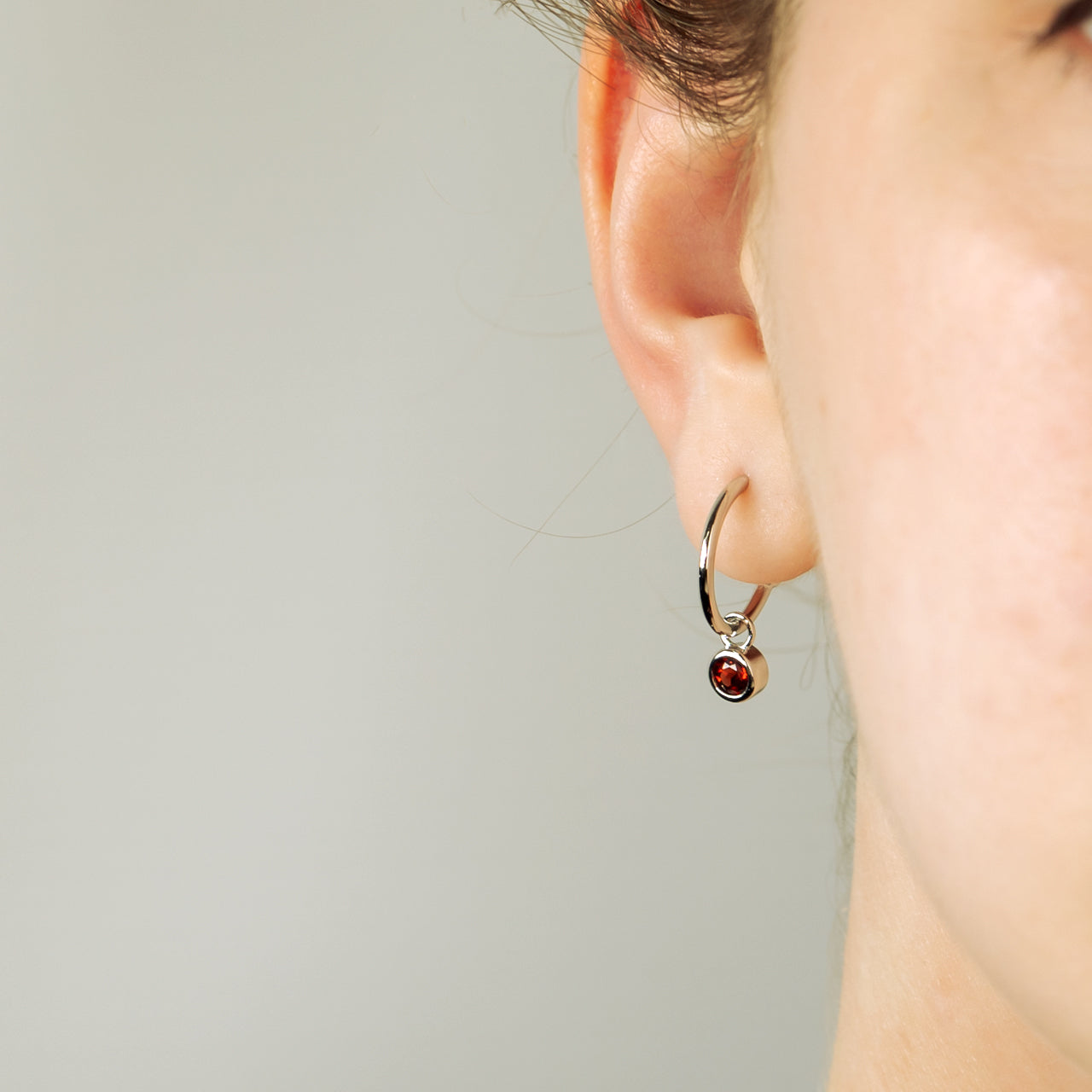 Delicate sterling silver hoop earrings featuring a deep red garnet birthstone, highlighting sculptural elegance from an award-winning British jeweller.