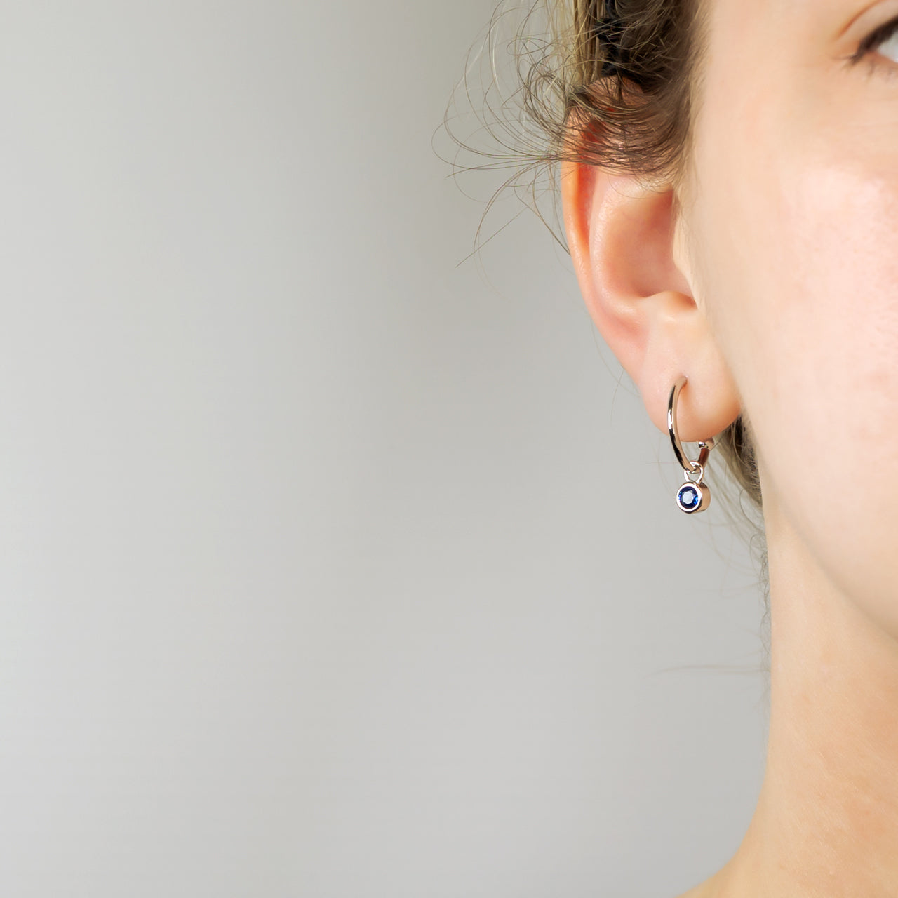 Delicate sterling silver hoop earring featuring a small blue spinel birthstone charm, showcasing expert British craftsmanship with a refined, sculptural design.