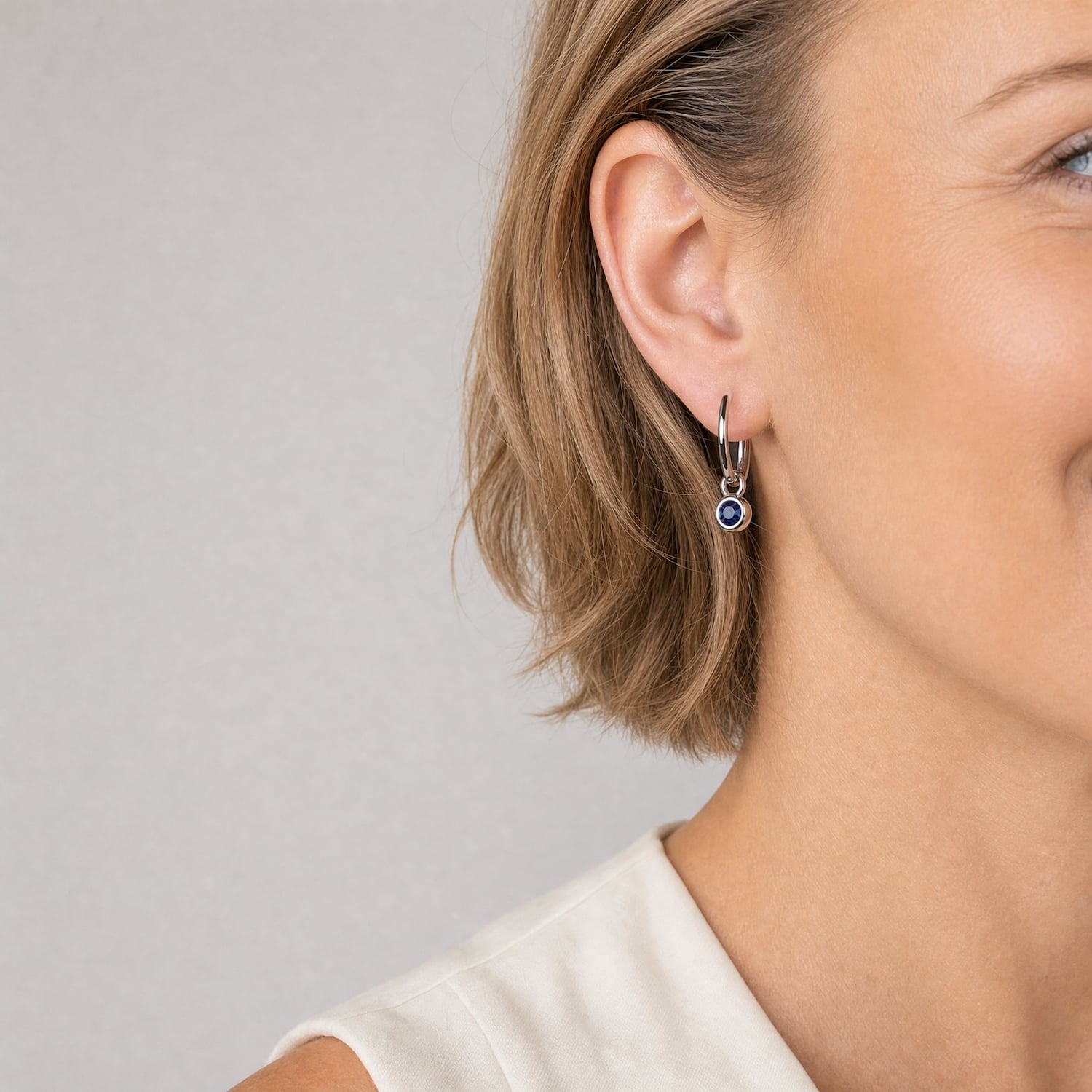 Close up of model wearing delicate sterling silver hoop earrings featuring a deep blue spinel gemstone, showcasing a sleek and sculptural design that reflects expert British craftsmanship.