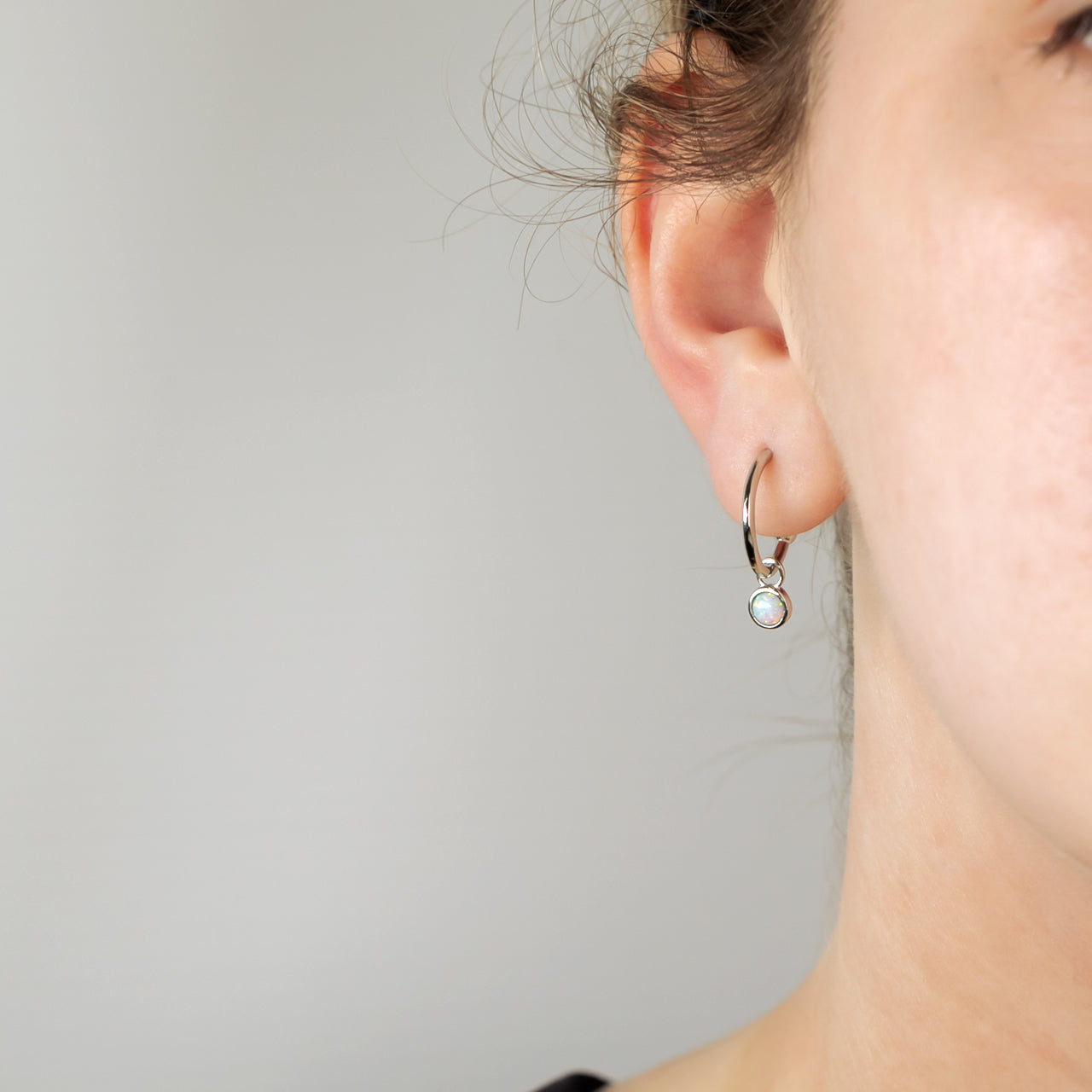 Delicate sterling silver hoop earrings featuring a small opal birthstone charm, showcasing refined craftsmanship and a minimalist, elegant design by Azendi.