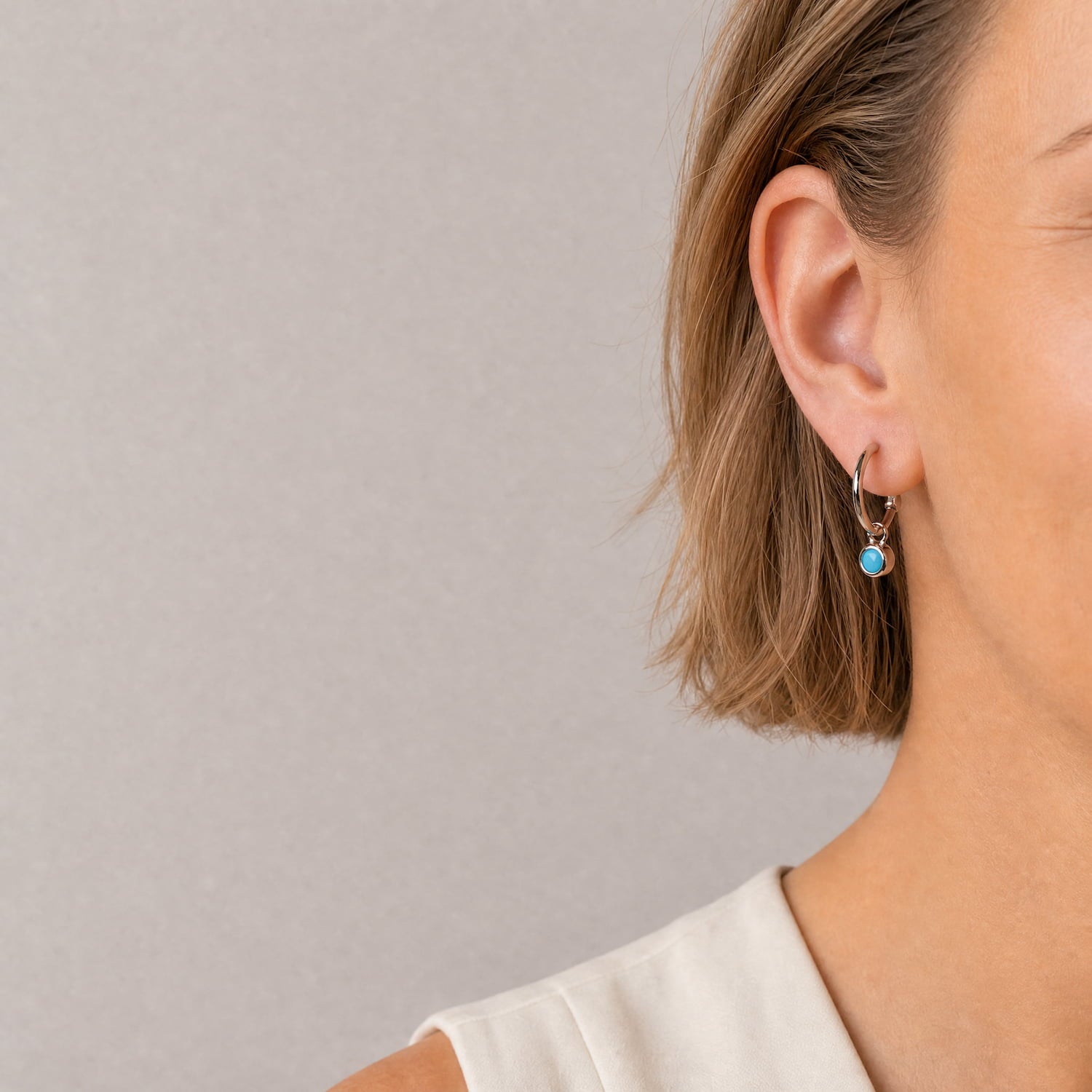 Delicate sterling silver hoop earrings featuring a small turquoise birthstone charm, highlighting a refined and expertly crafted design by a British jeweller.