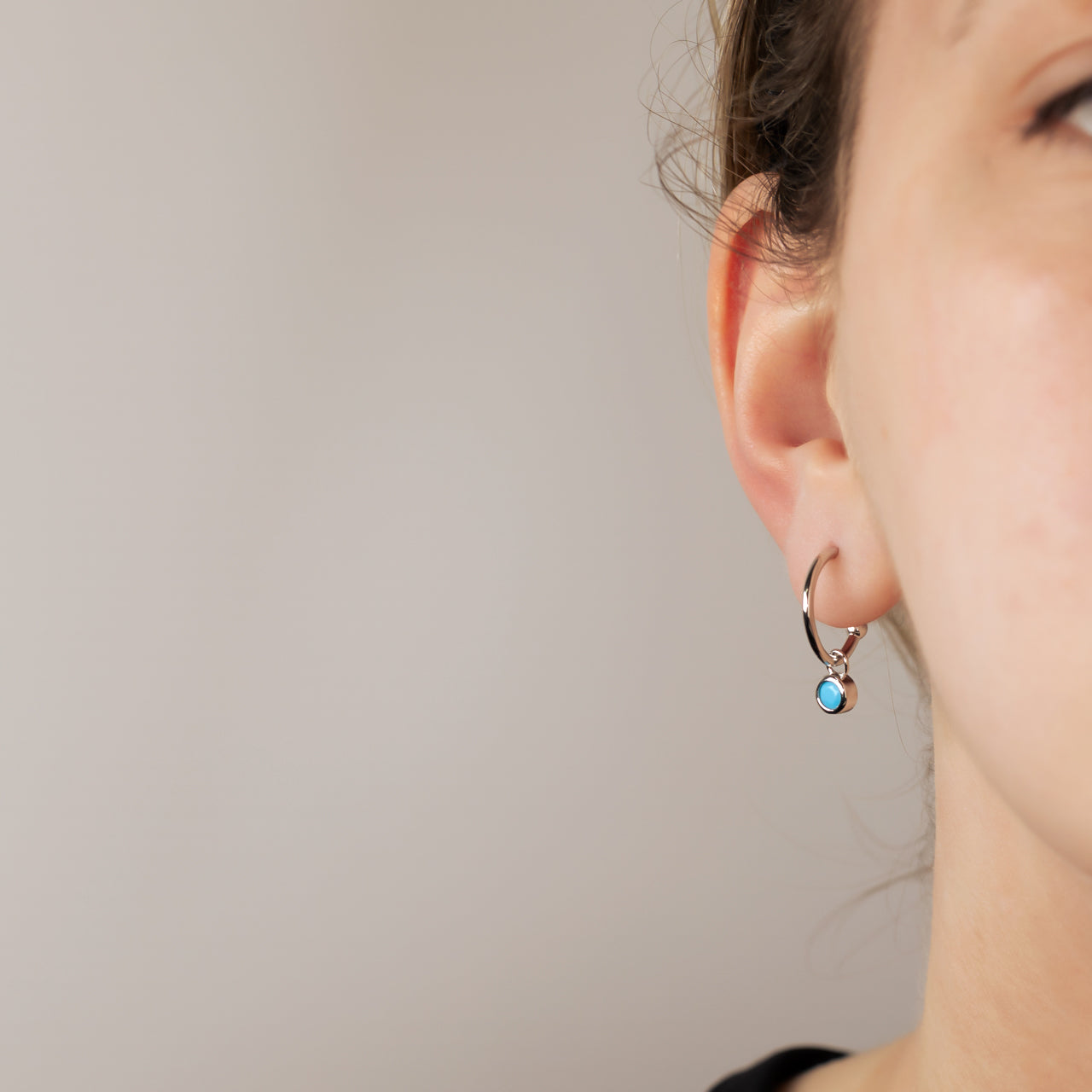 Delicate sterling silver hoop earrings featuring a small turquoise birthstone charm, highlighting a refined and expertly crafted design by a British jeweller.