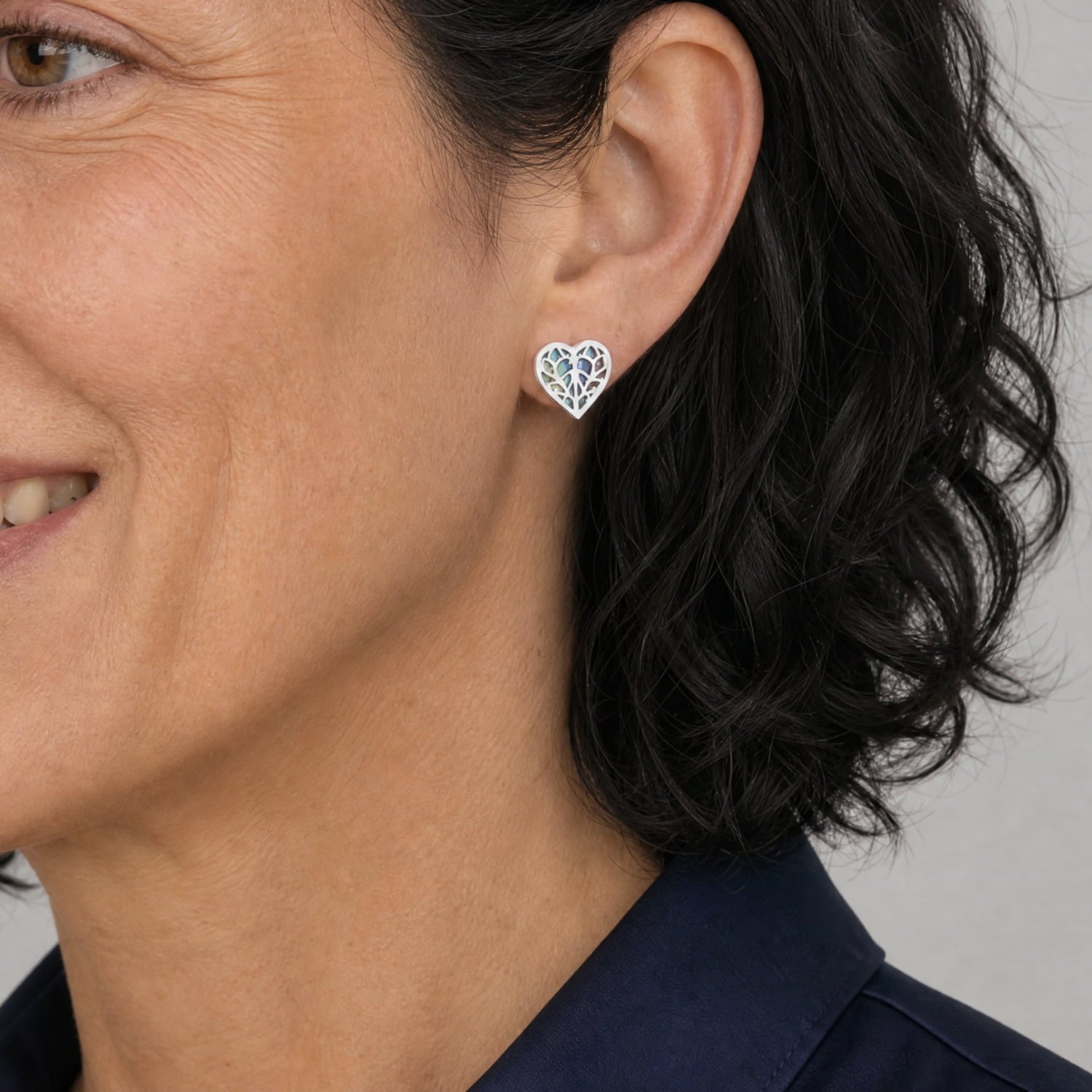 Model wears a pair of 9 carat white gold stud earrings featuring heart-shaped openwork design with iridescent abalone inlay, combining sculptural elegance with a contemporary finish.