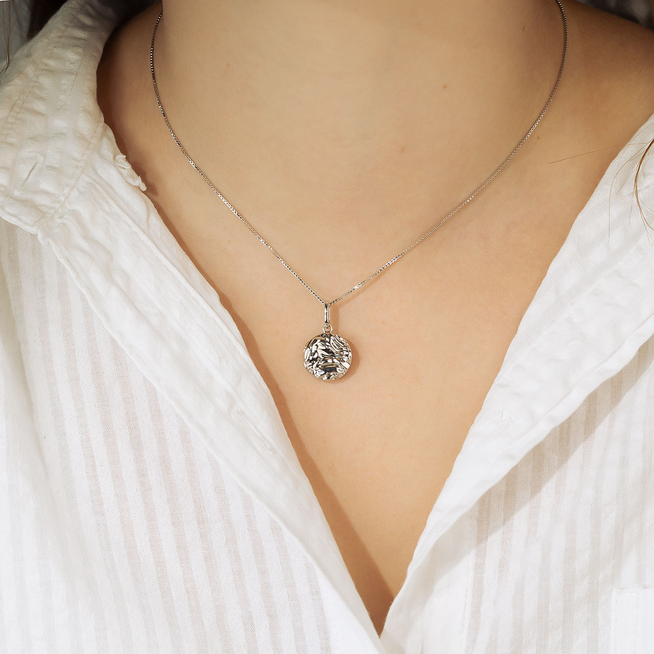 Close-up of a sterling silver textured wave pendant on an adjustable chain, styled with a white shirt to showcase its modern and sculptural design by Azendi.