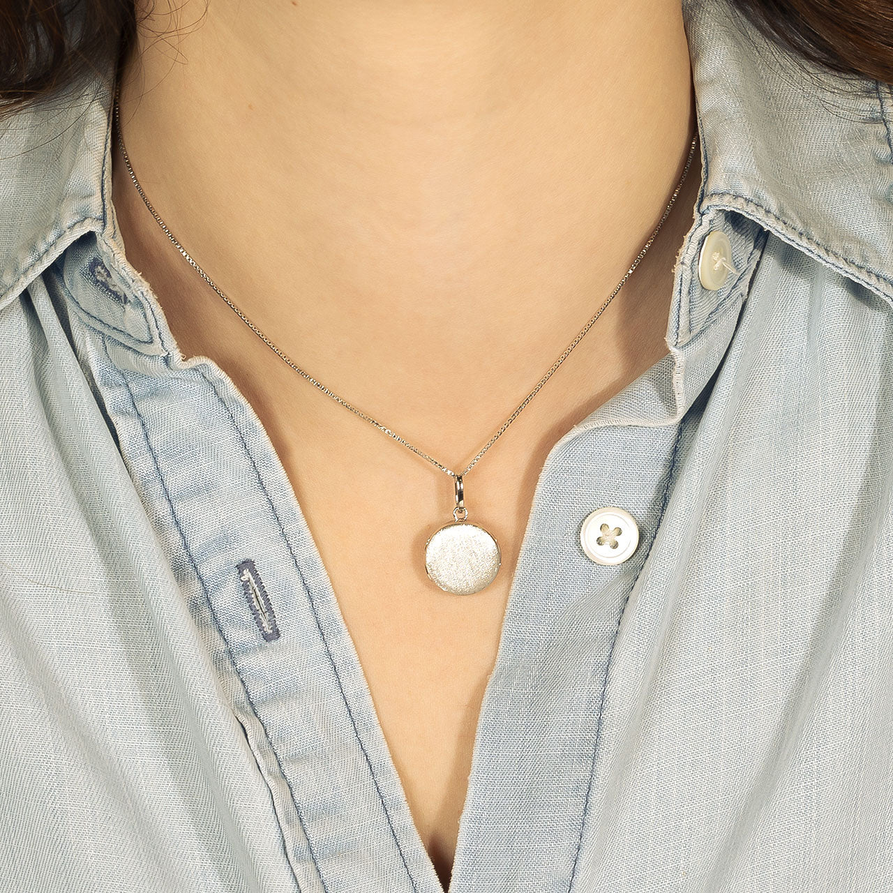 Close-up of a wearer showcasing a sterling silver satin-finished round locket pendant on a delicate adjustable chain, highlighting its sculptural and contemporary design.