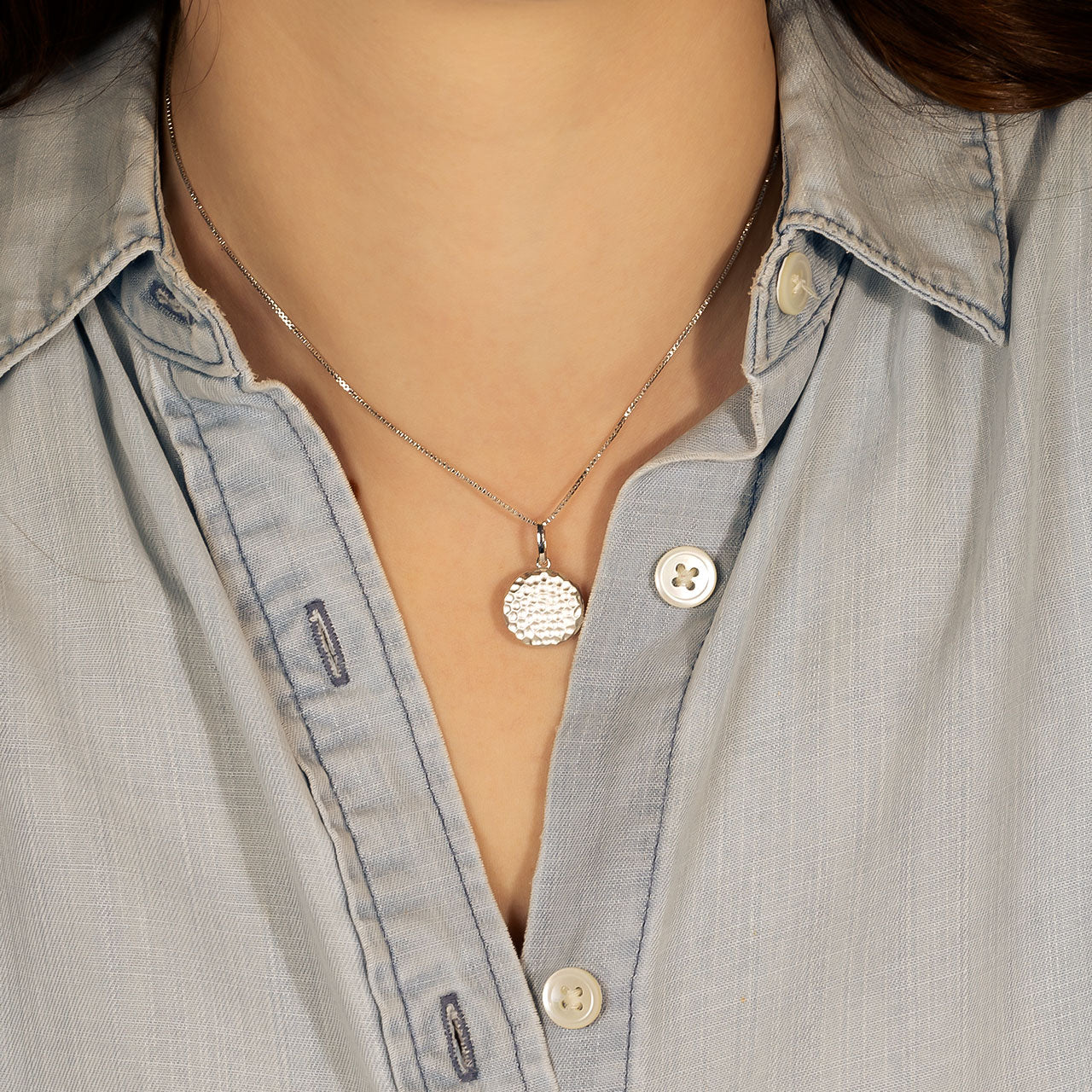 Close-up of a sterling silver pendant with a satin hammered texture on an adjustable fine chain, worn with a light blue shirt for a refined, contemporary look.