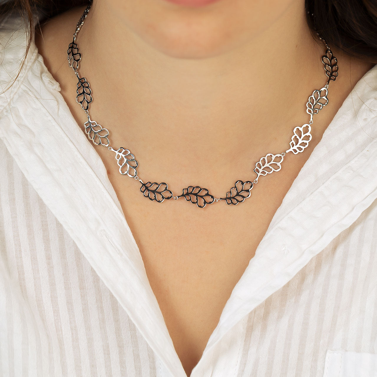 Sterling silver necklace featuring linked oak leaf motifs with an openwork design, worn against a white textured blouse for a natural, sculptural look.